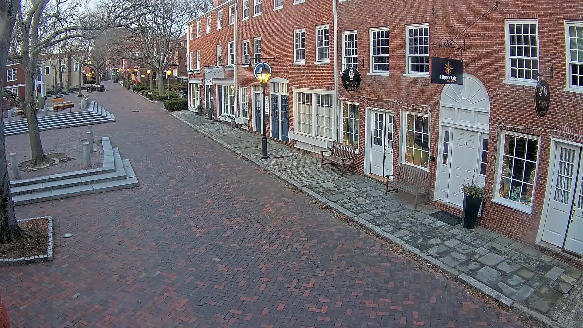 A brick-paved street lined with brick buildings on a partly cloudy day.