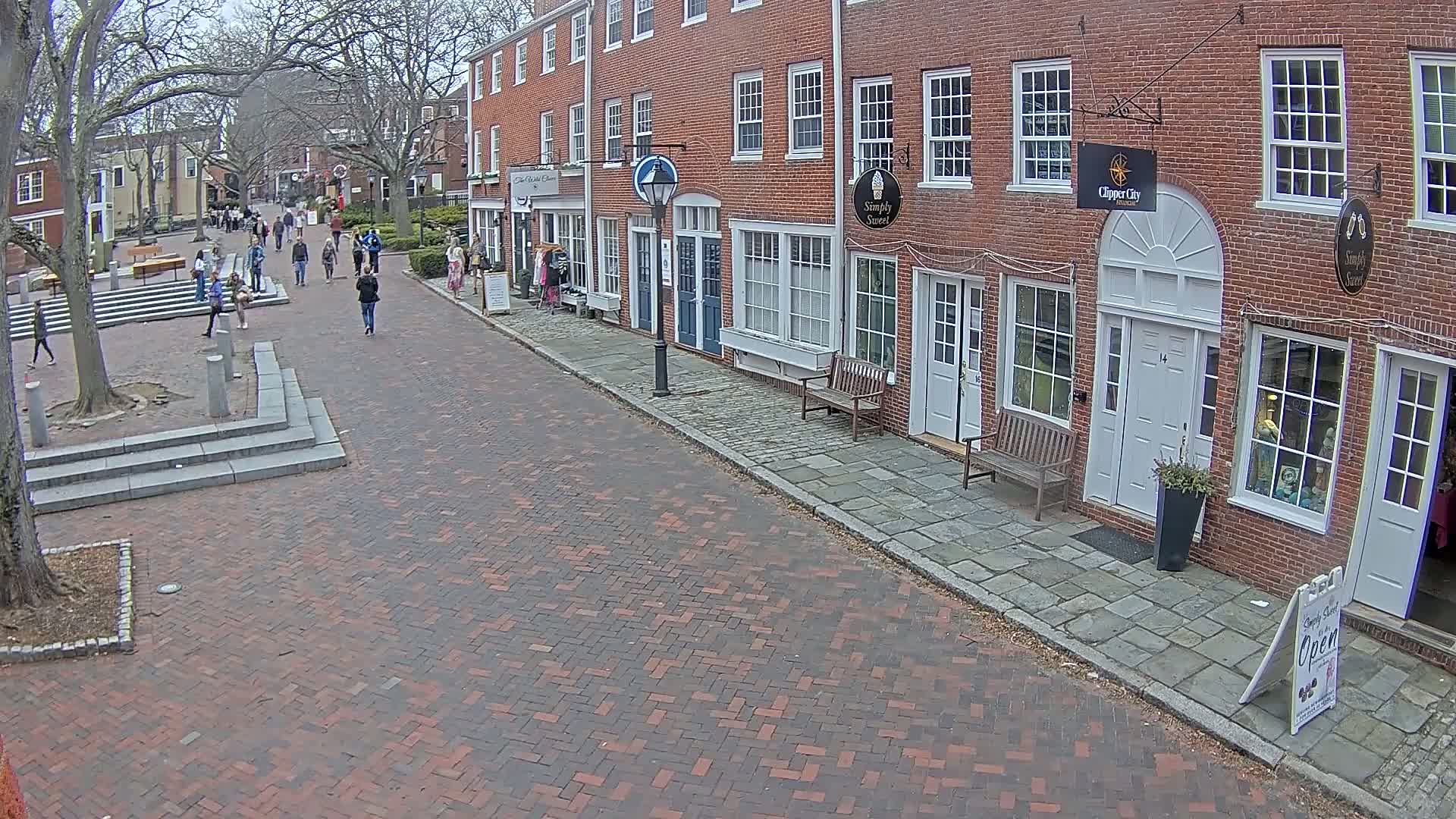 A brick-paved street lined with brick buildings and several pedestrians, under an overcast sky.