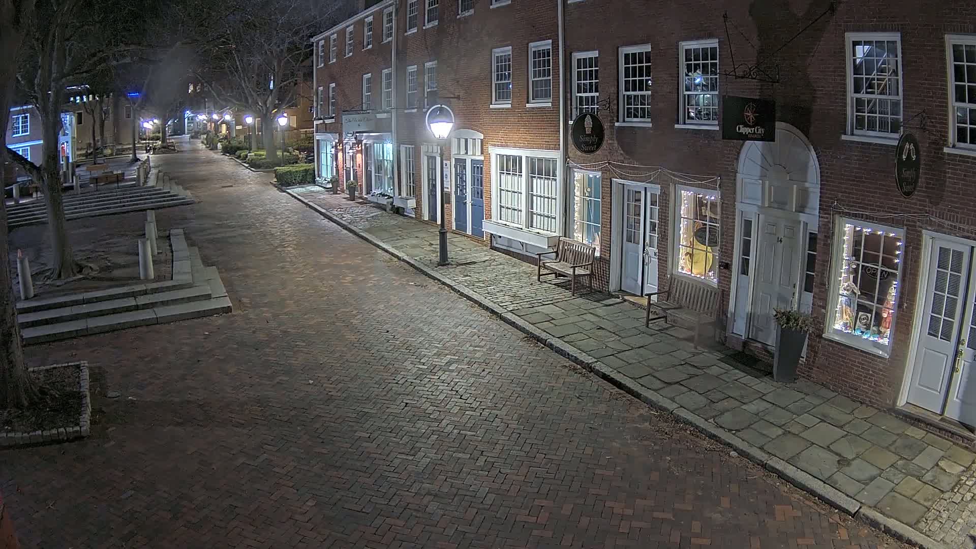 A brick street lined with brick buildings at night, lit by streetlights.
