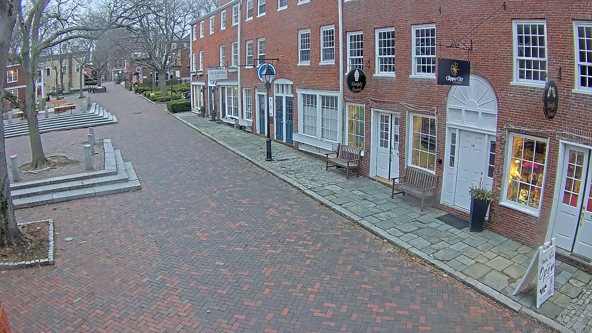 A brick-paved street lined with brick buildings and trees, under an overcast sky.