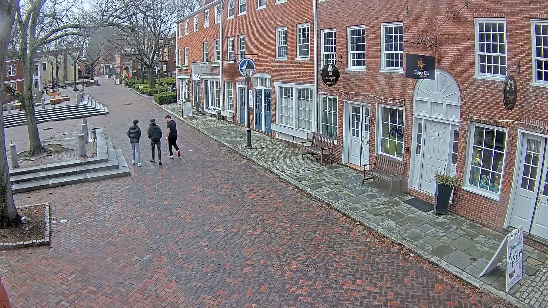 Three people walk down a brick street lined with brick buildings on a cloudy day.