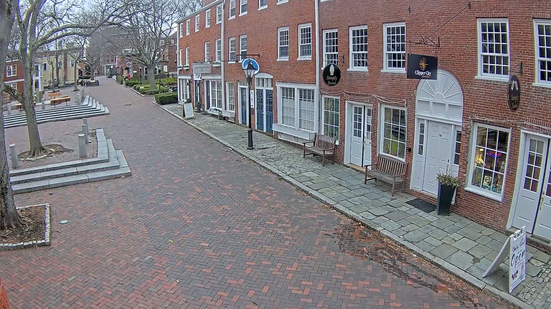 A brick street lined with brick buildings, some with shops, on an overcast day.