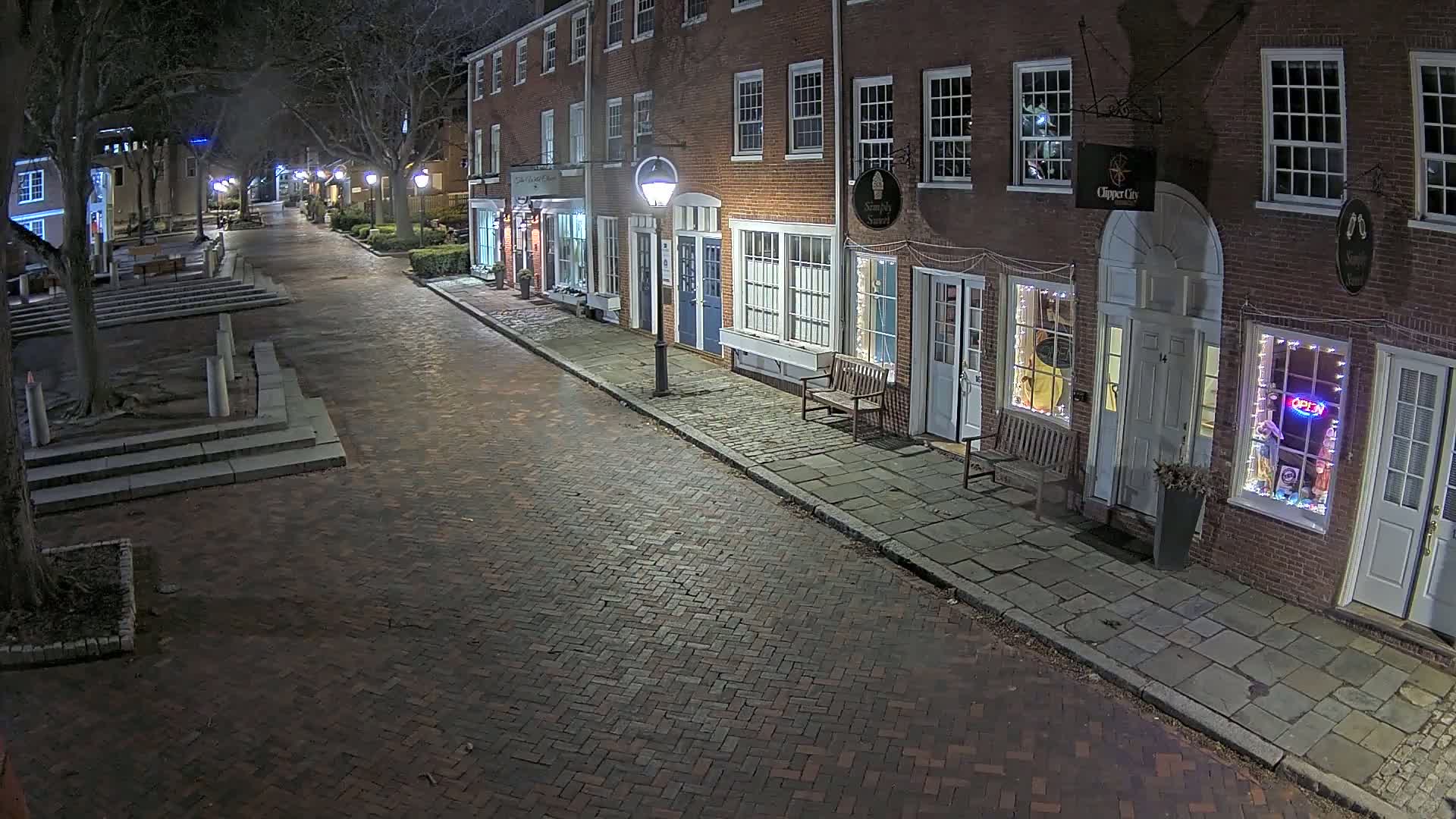 A brick street at night, lined with brick buildings, is illuminated by streetlights.