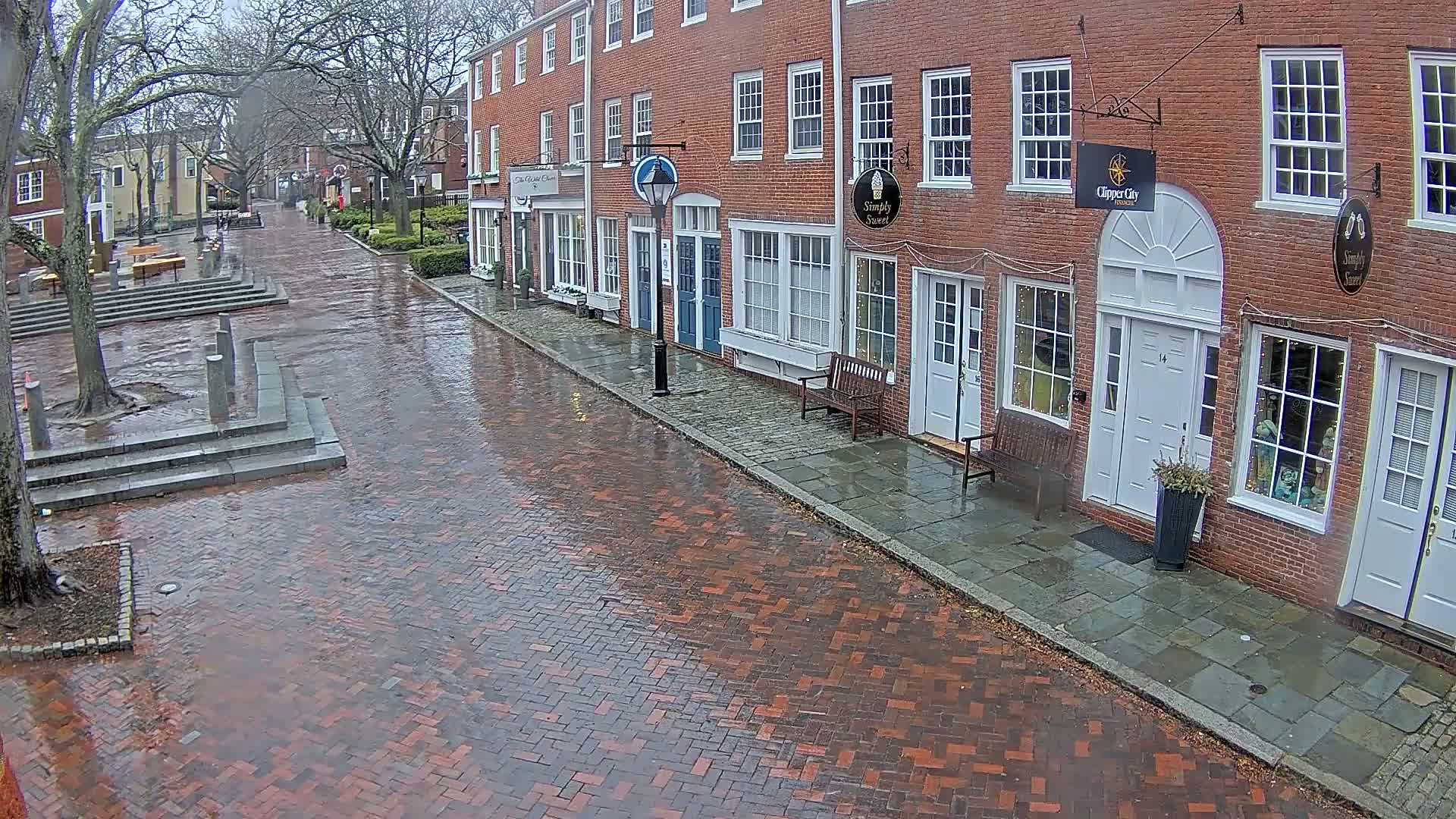 A wet brick street lined with brick buildings on a cloudy day.