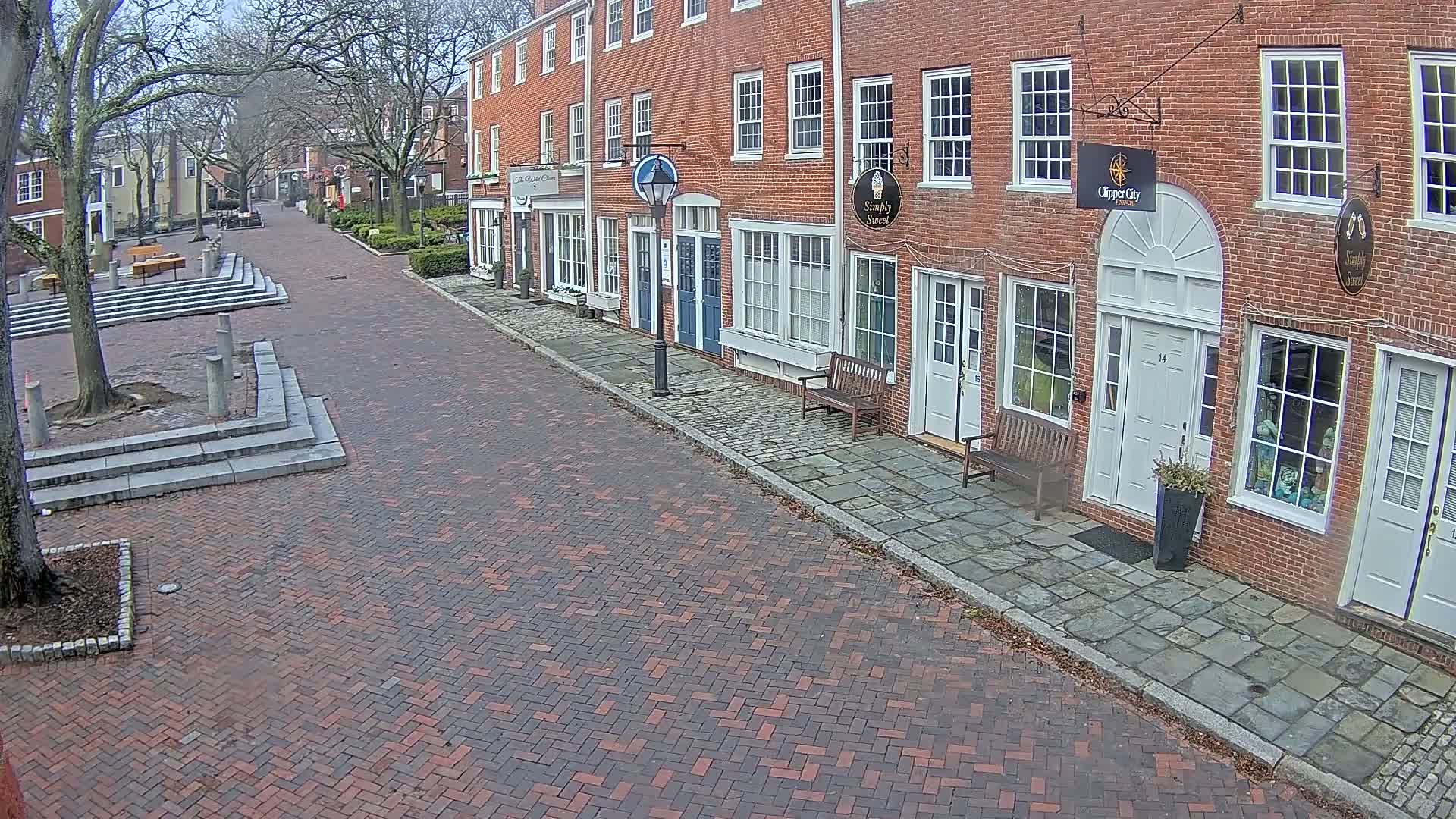 A brick street lined with brick buildings on a cloudy day, with a small square visible in the background.