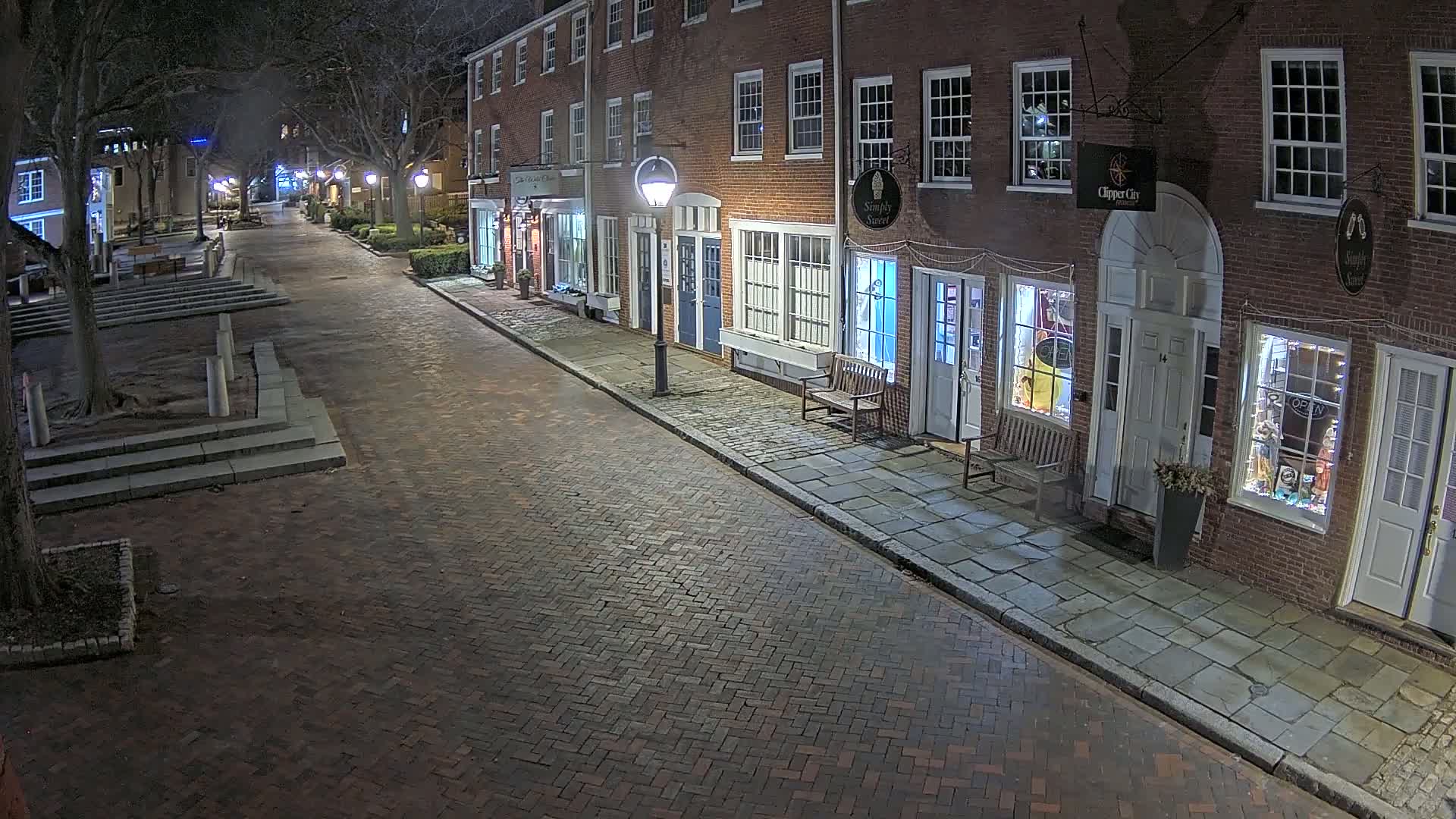 A brick street lined with brick buildings at night, illuminated by streetlights.