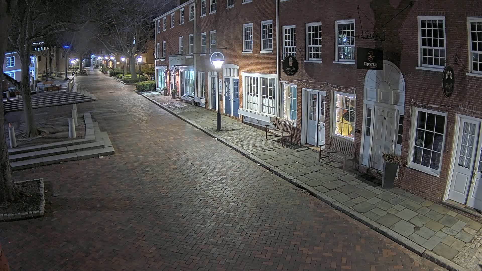 A brick street lined with brick buildings at night, illuminated by streetlights.