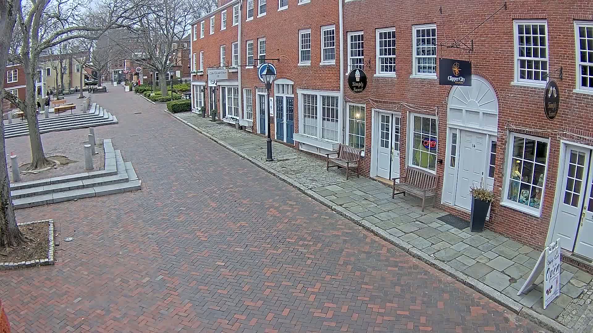 A brick street lined with brick buildings on a cloudy day leads to a small plaza with stairs.