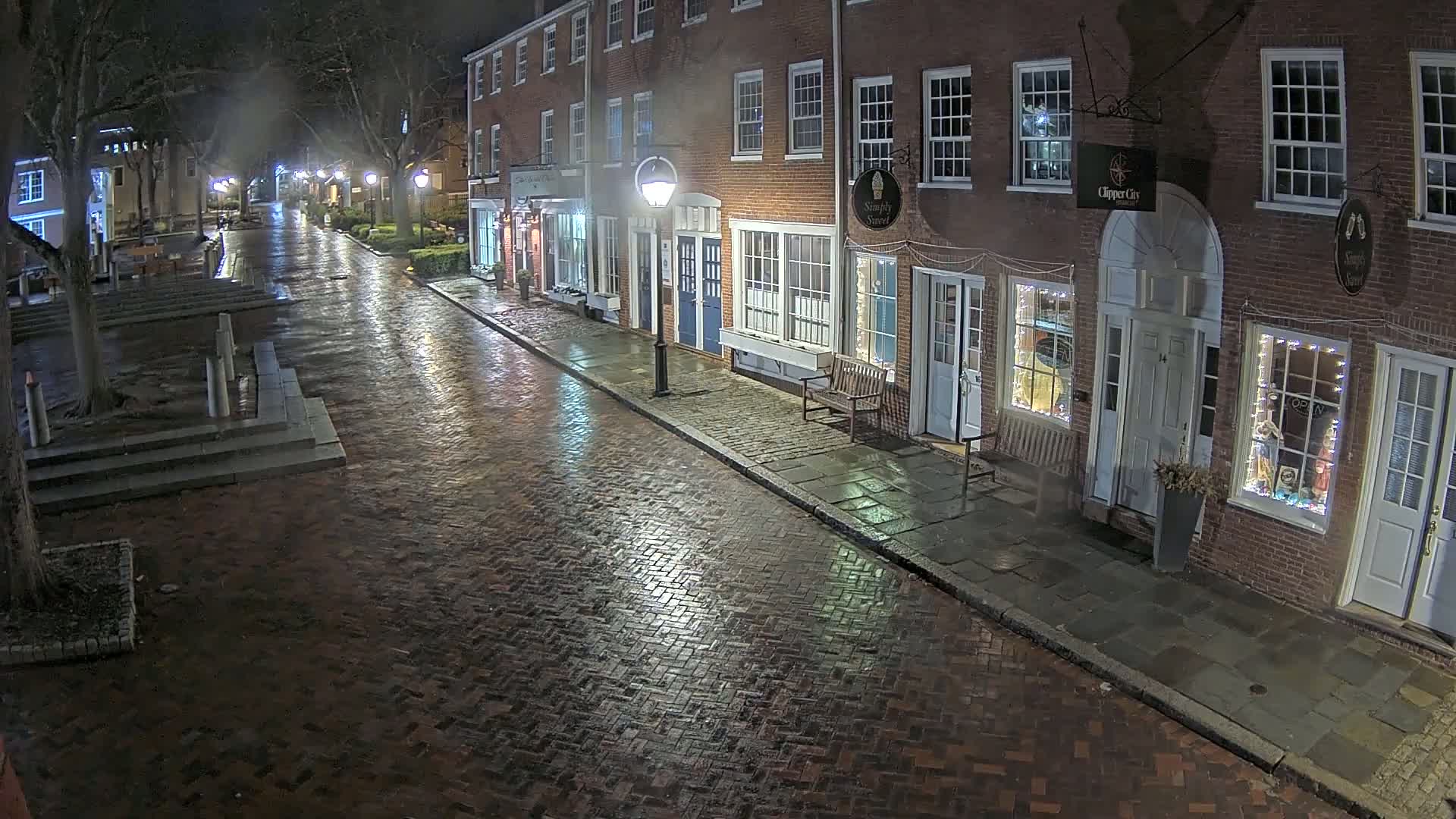 A wet brick street at night, lined with brick buildings and illuminated by streetlights.