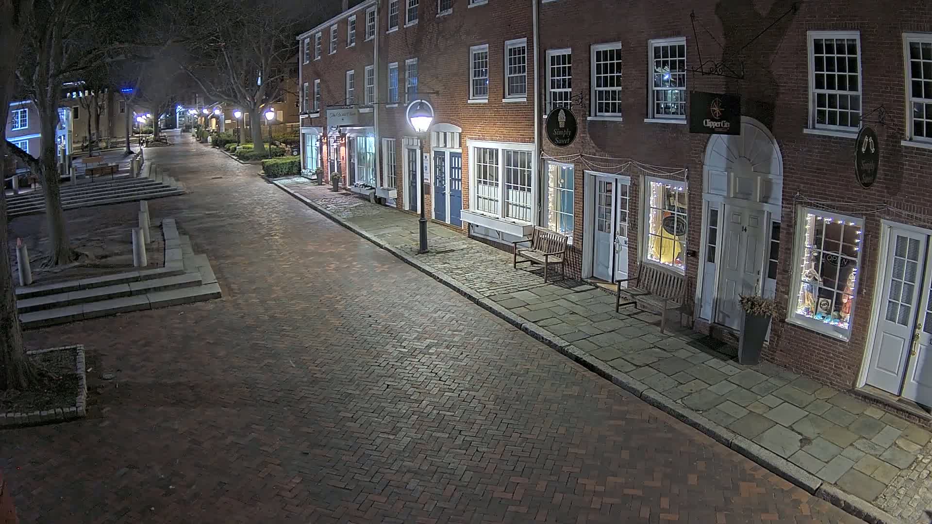 A brick street at night lined with illuminated storefronts in a row of brick buildings.