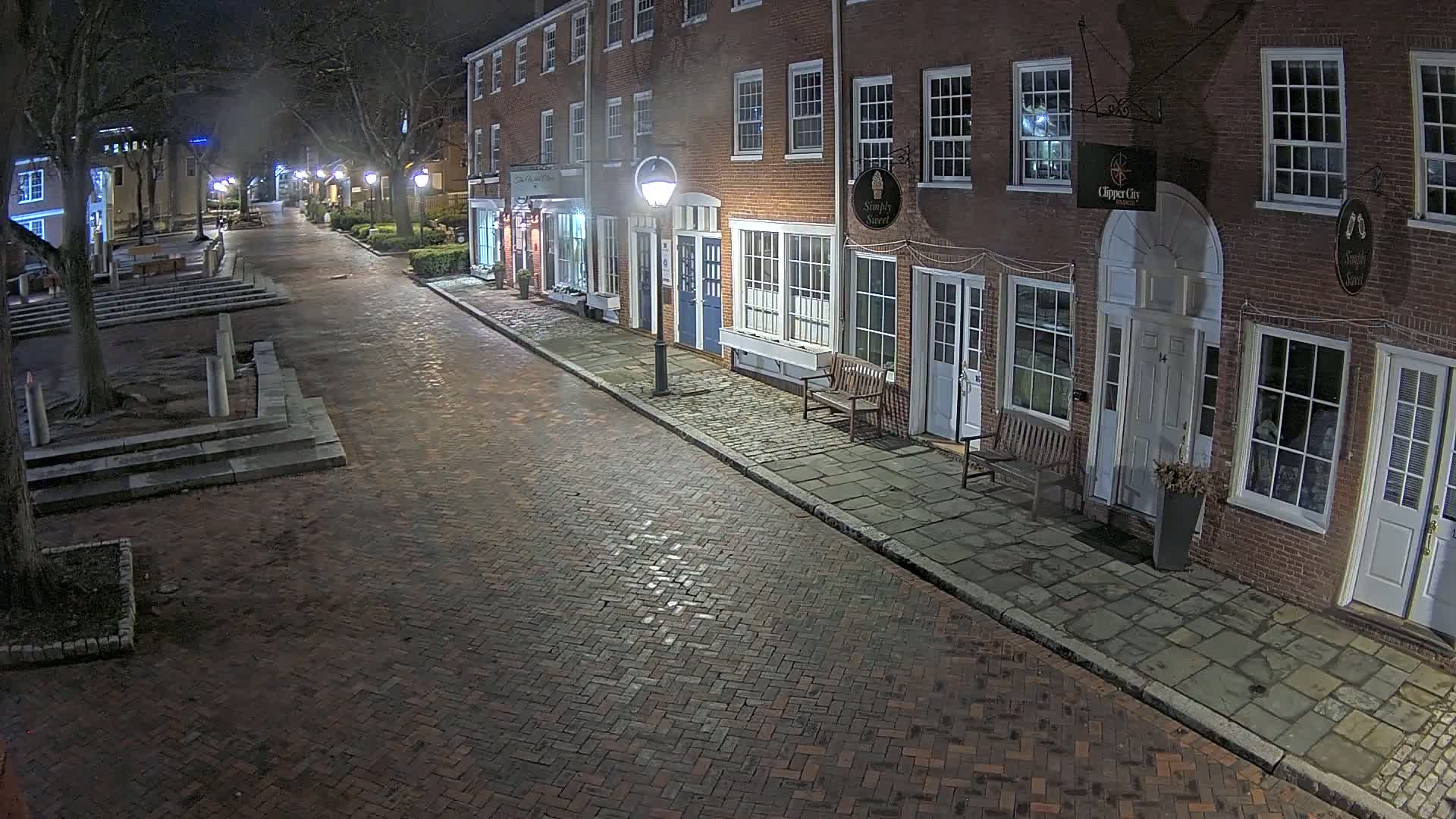 A brick street lined with brick buildings at night, lit by street lamps.