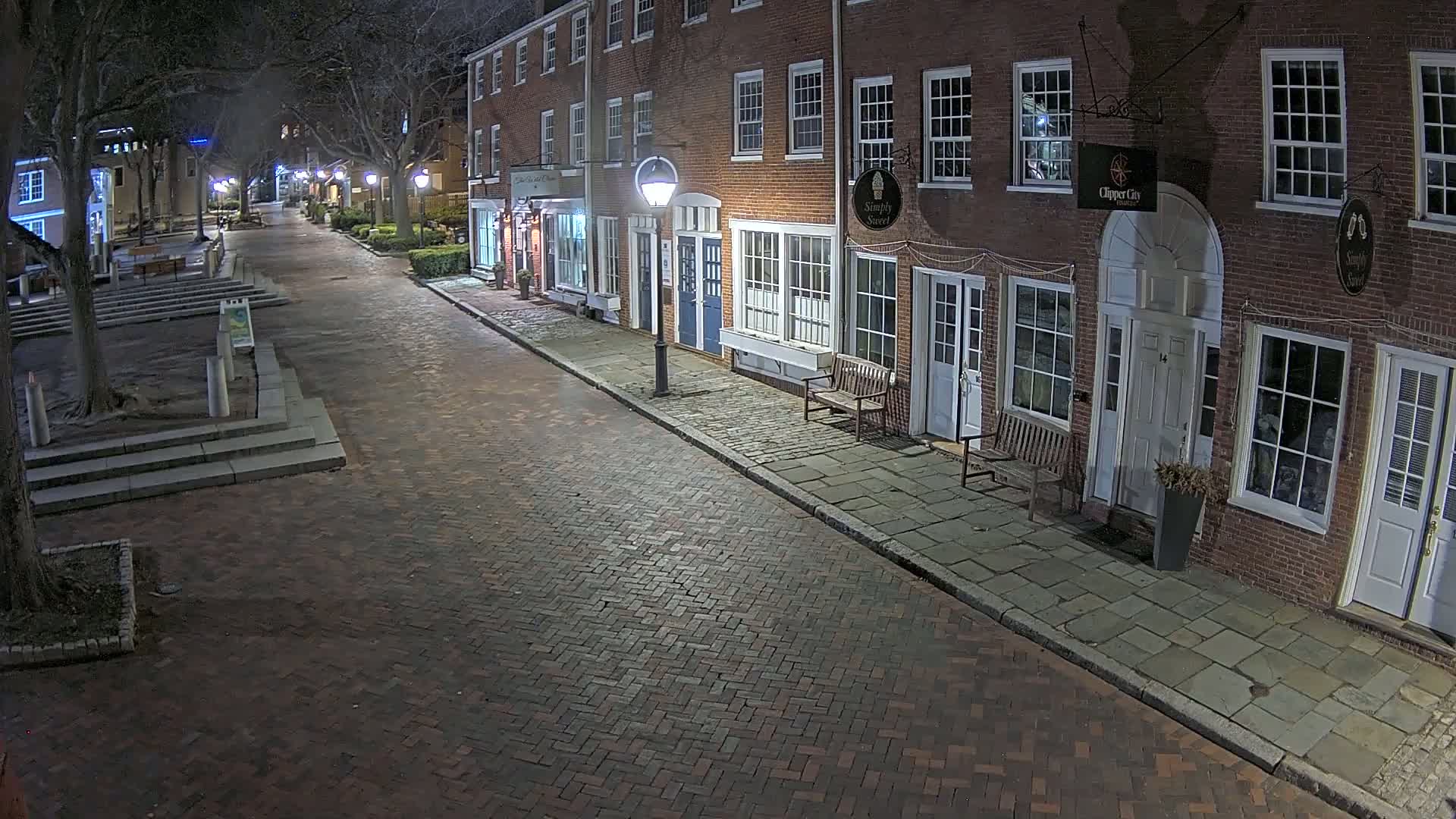 A brick street at night lined with brick buildings, lit by street lamps.