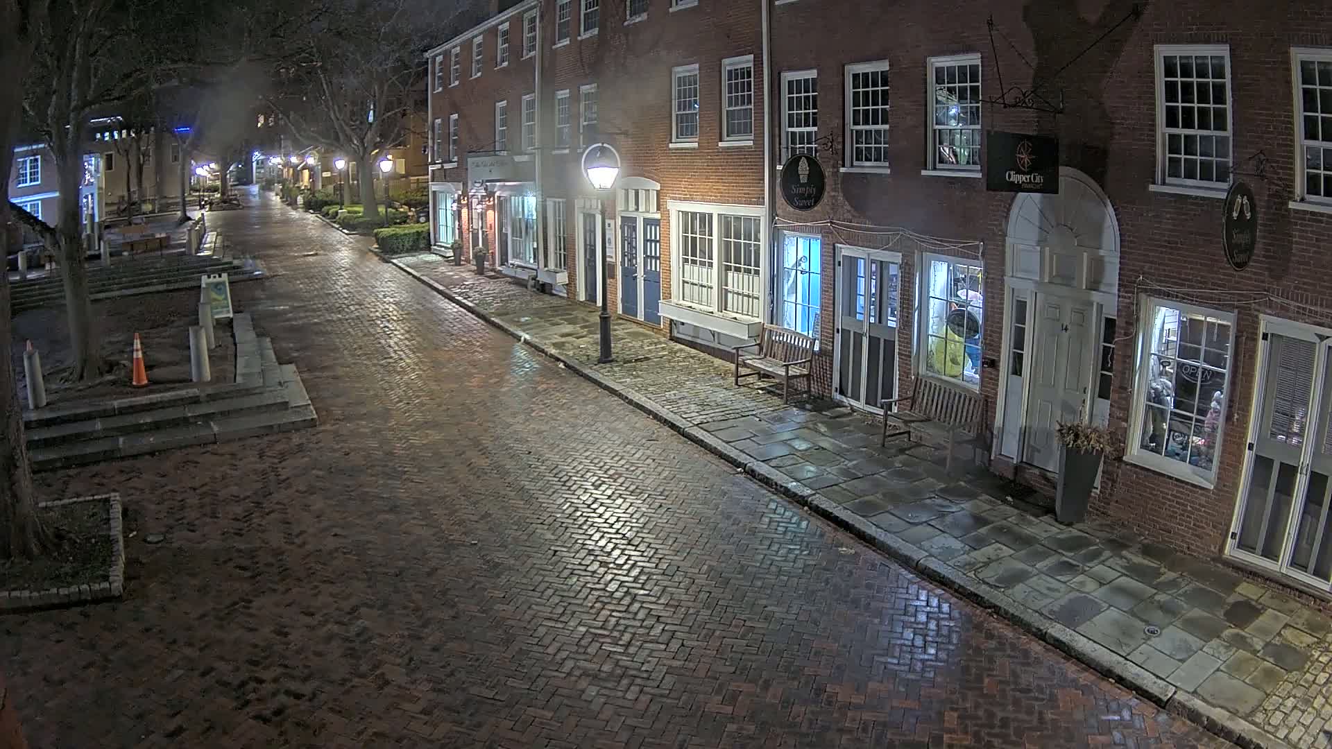A wet brick street at night is lined with brick buildings, each with multiple lit windows.