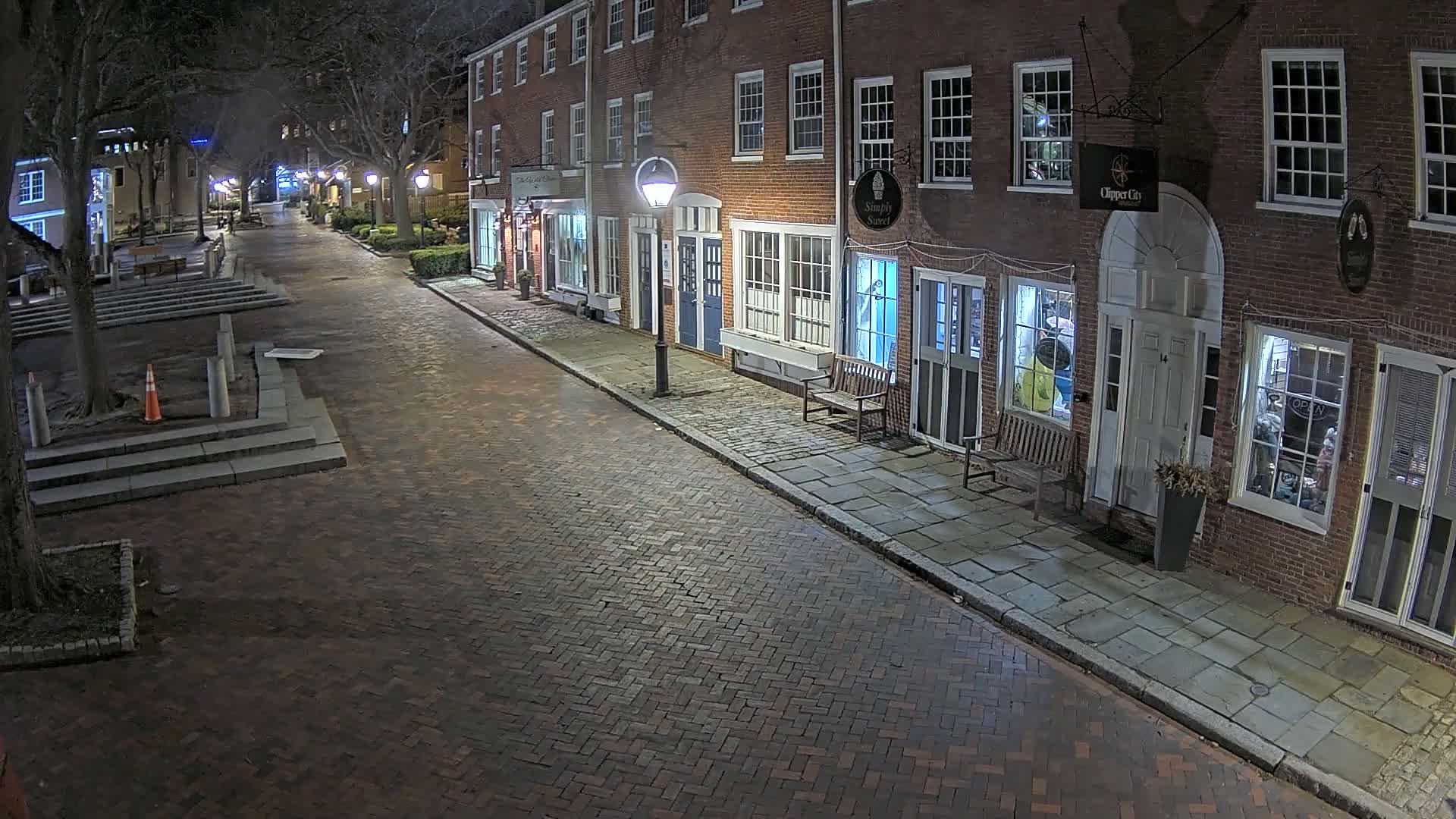A brick street lined with brick buildings at night, illuminated by streetlights.