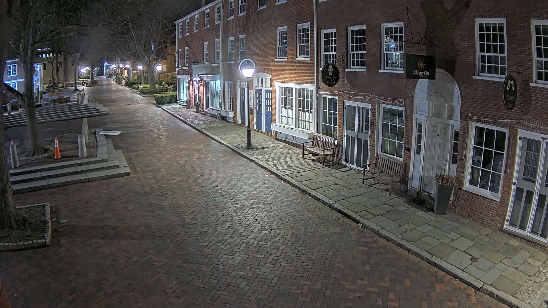 A brick street at night, lined with brick buildings, is lit by streetlights.