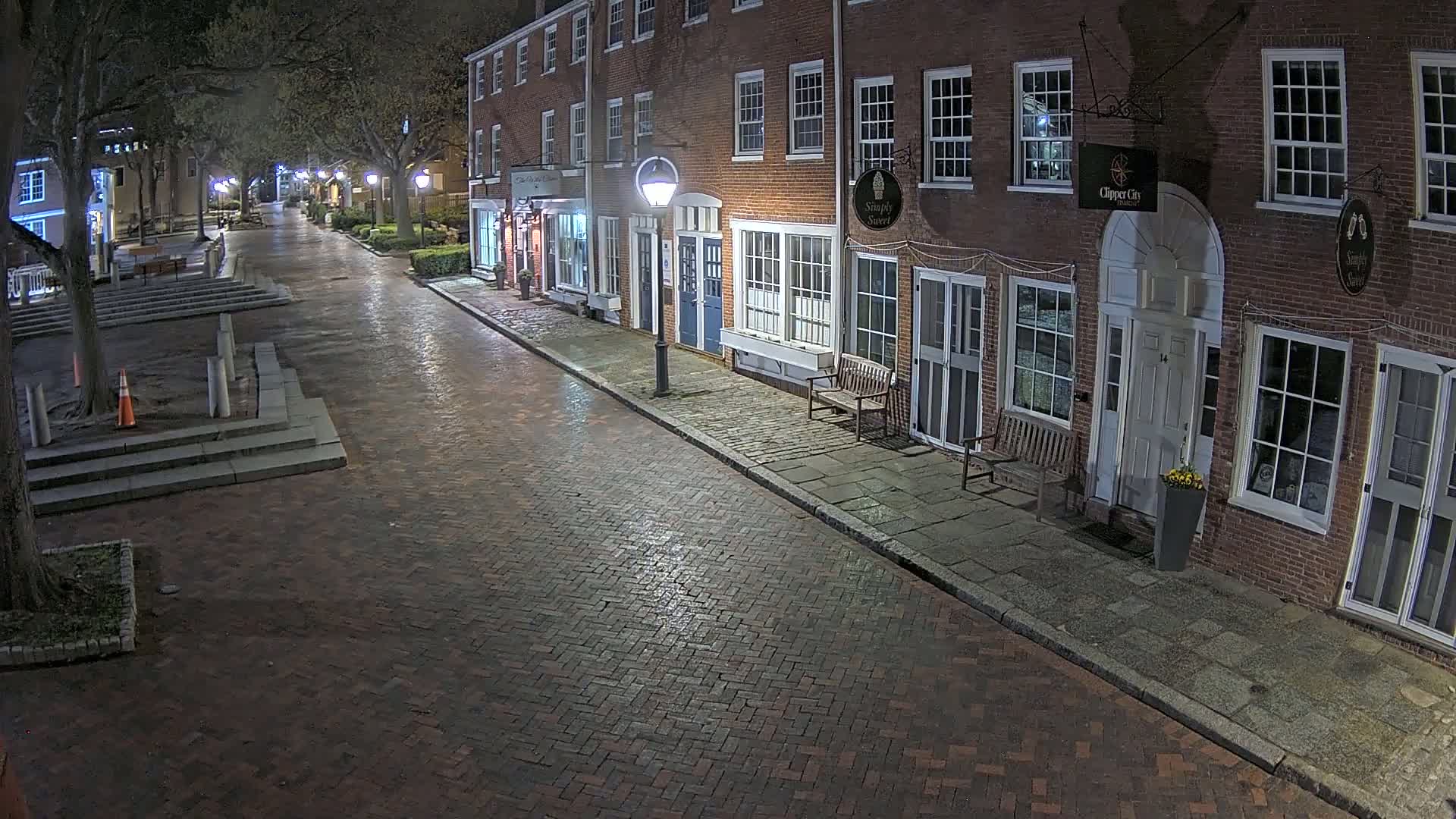A wet brick street at night is lined with brick buildings, illuminated by streetlights.