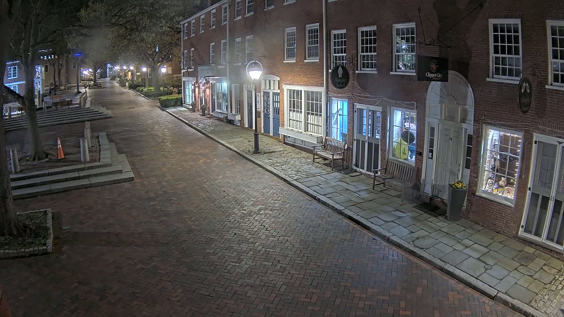 A brick-paved street at night lined with brick buildings, lit by street lamps, under a clear, dark sky.