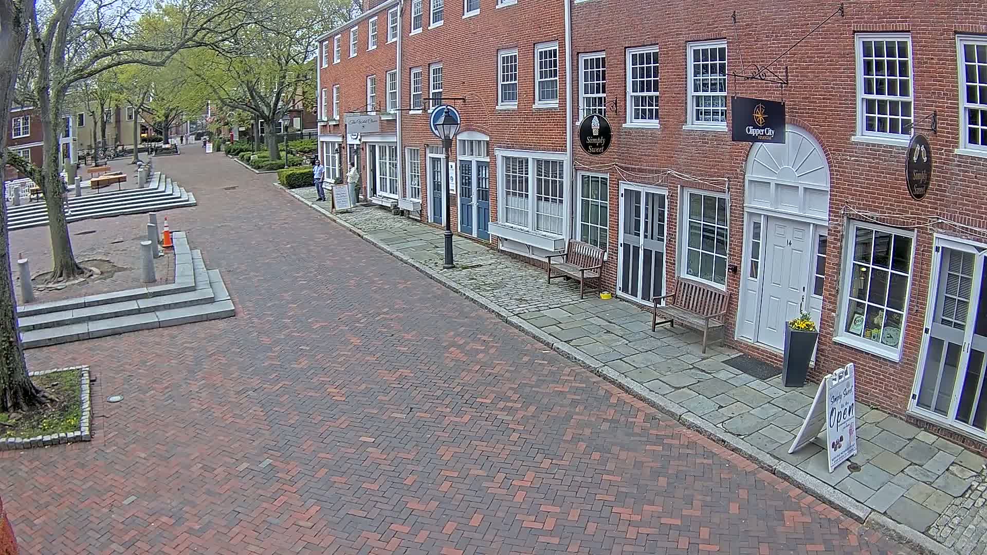 A brick-paved street lined with brick buildings on a partly sunny day.