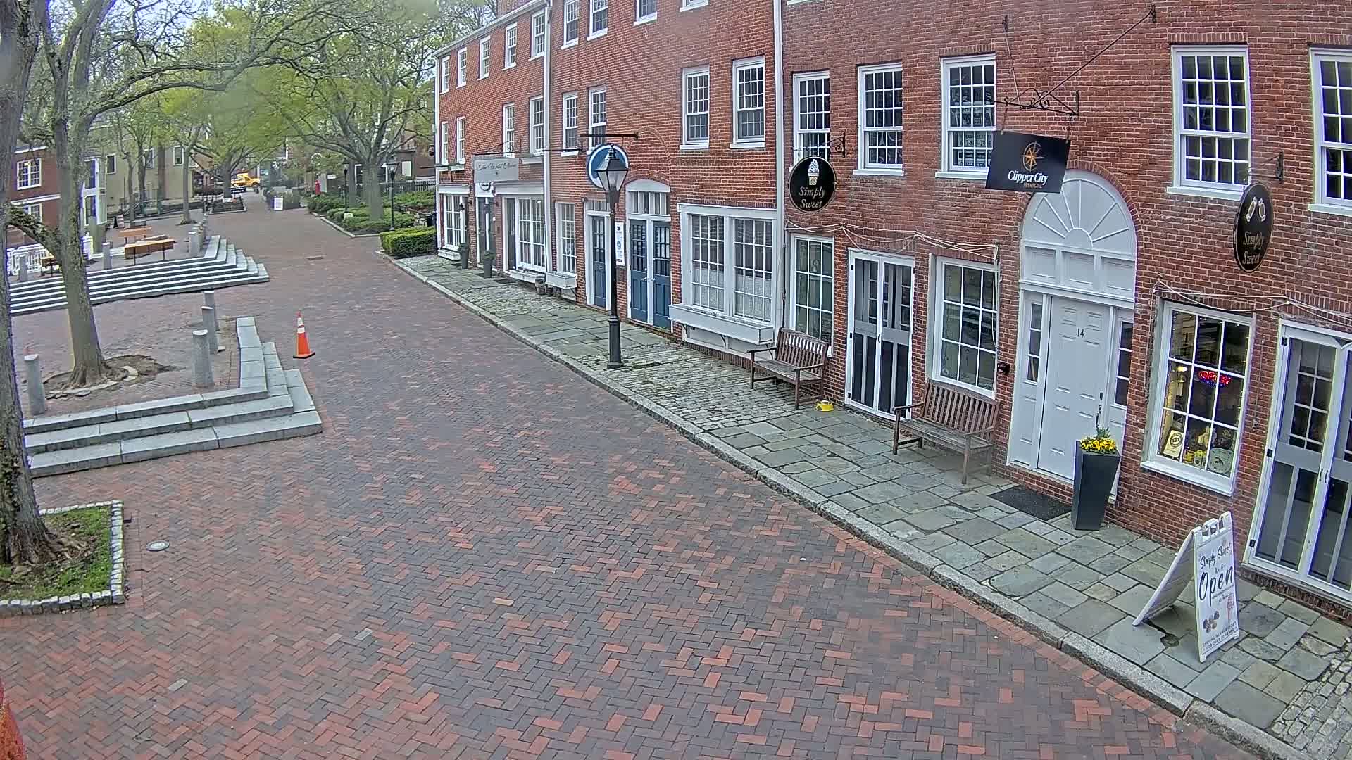A brick-paved street lined with brick buildings on a partly cloudy day leads to a small plaza with tiered steps.