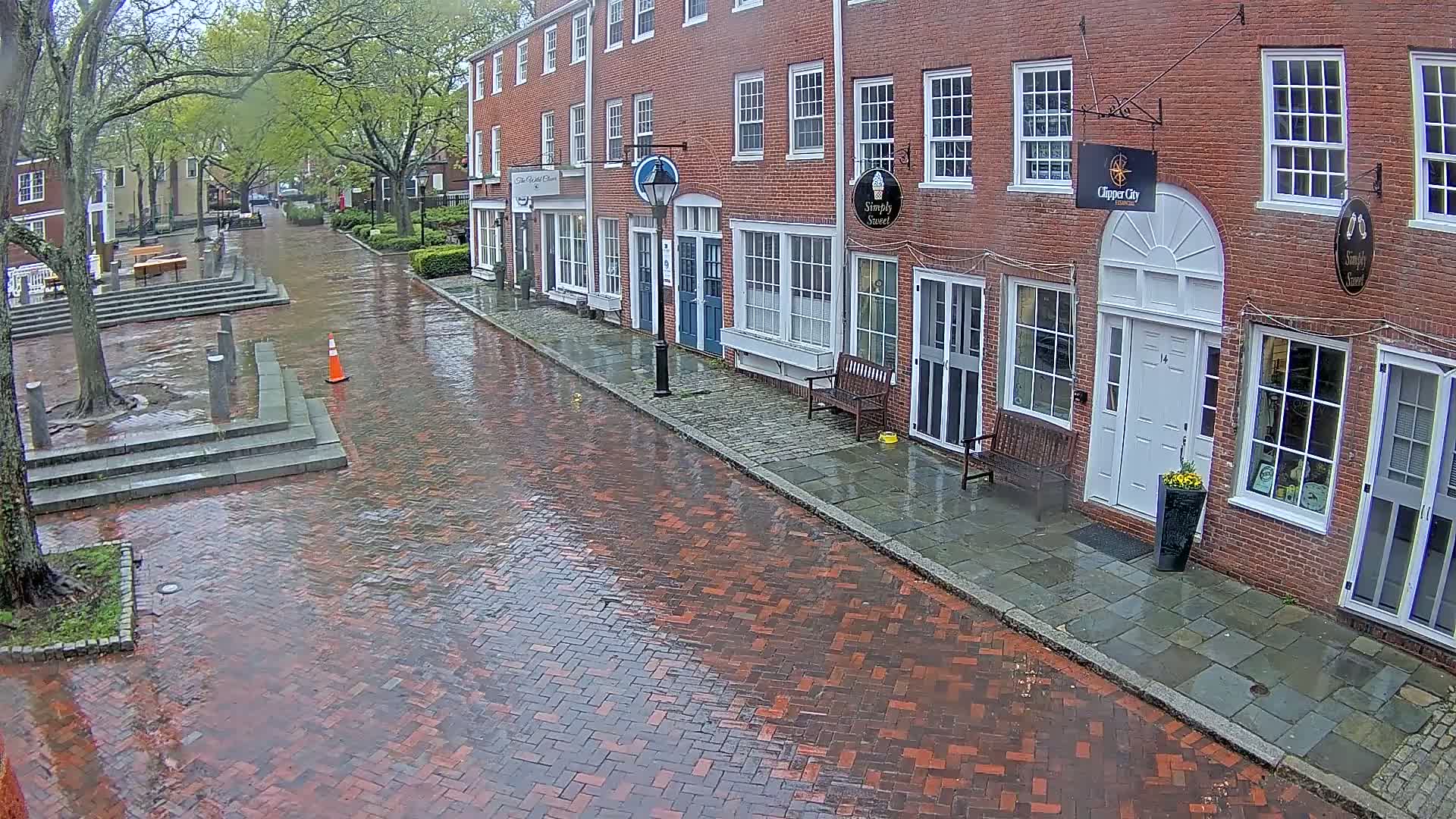 A wet, brick-paved street lined with brick buildings under a cloudy sky.