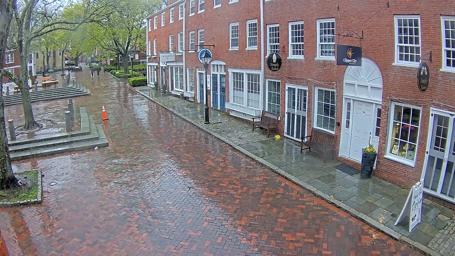 A wet brick street lined with brick buildings under a cloudy sky.