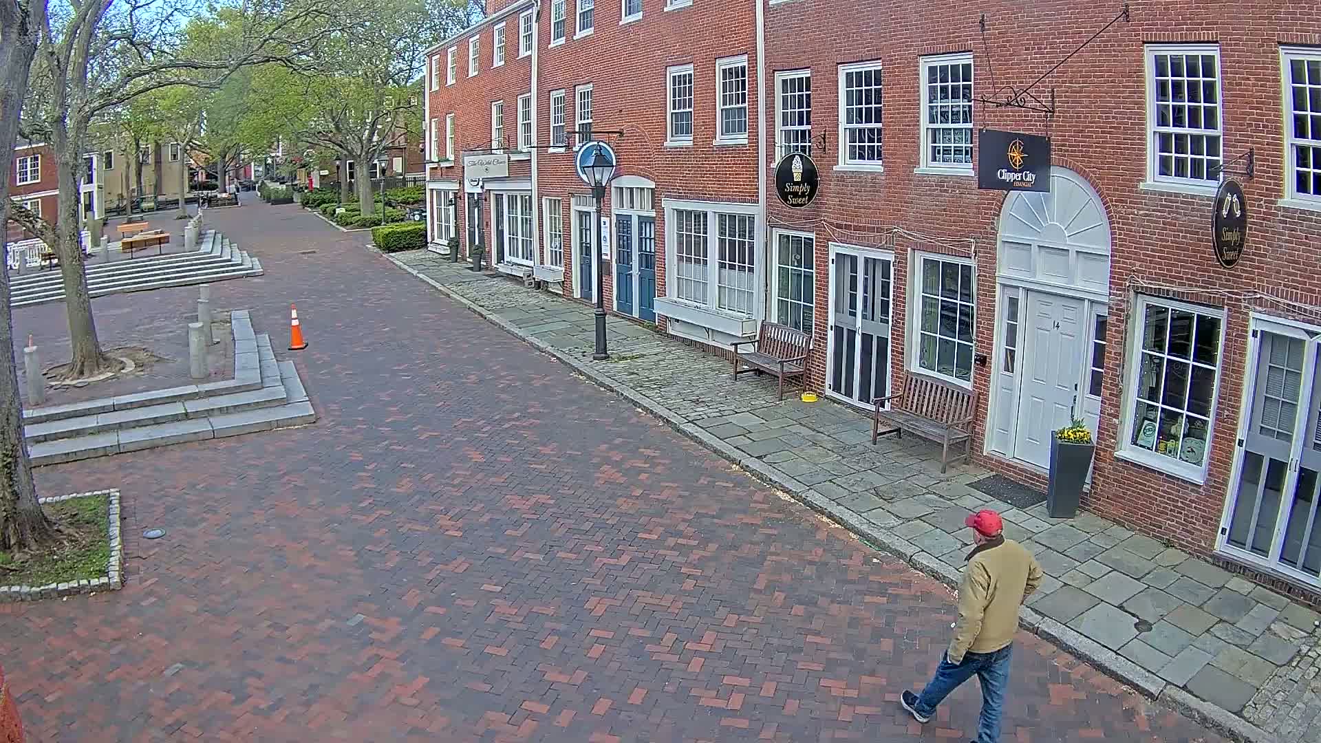 A man walks down a brick-paved street lined with brick buildings under a partly cloudy sky.