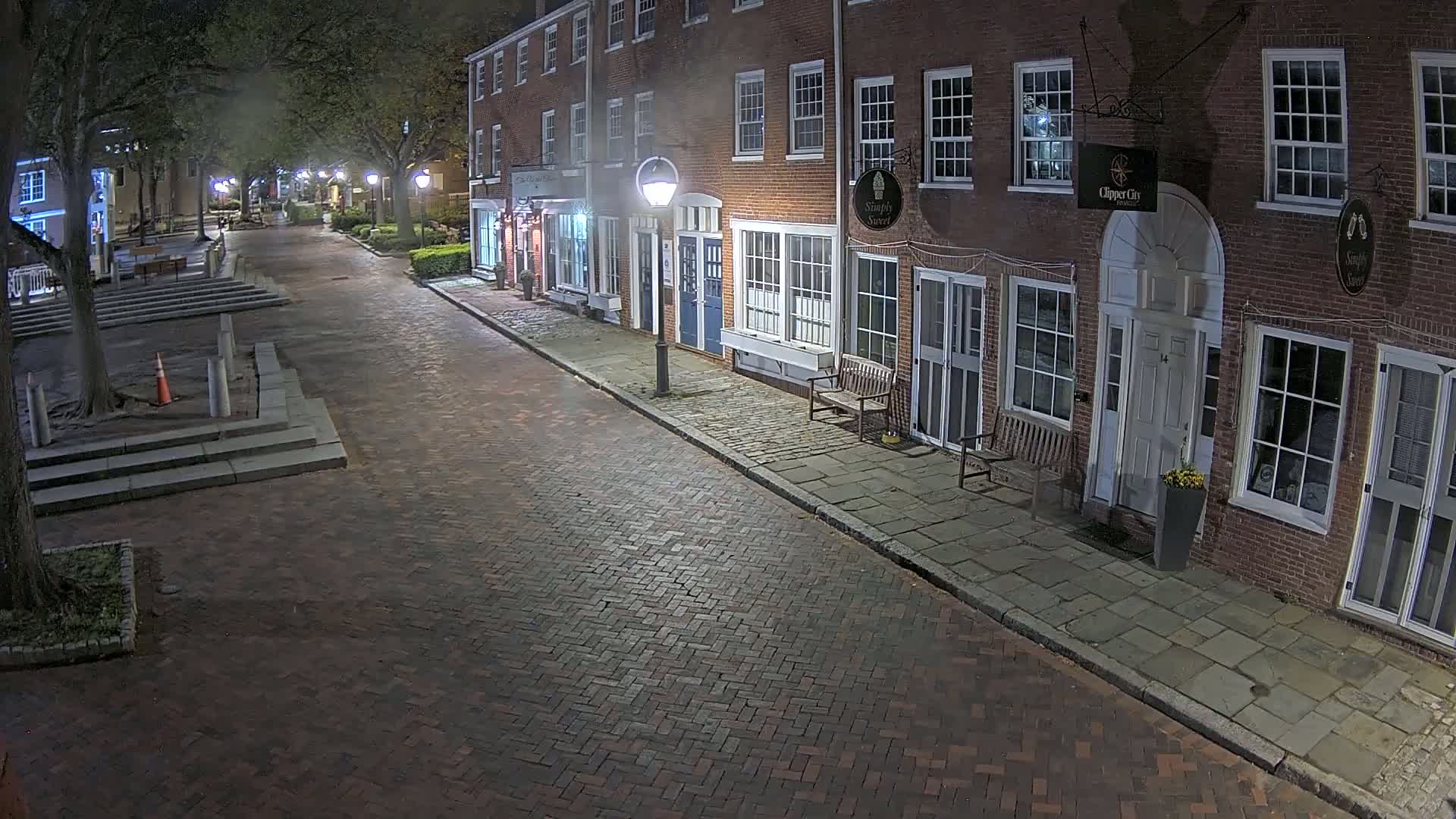 A brick street at night, lined with brick buildings and illuminated by streetlights, shows a quiet, empty scene.