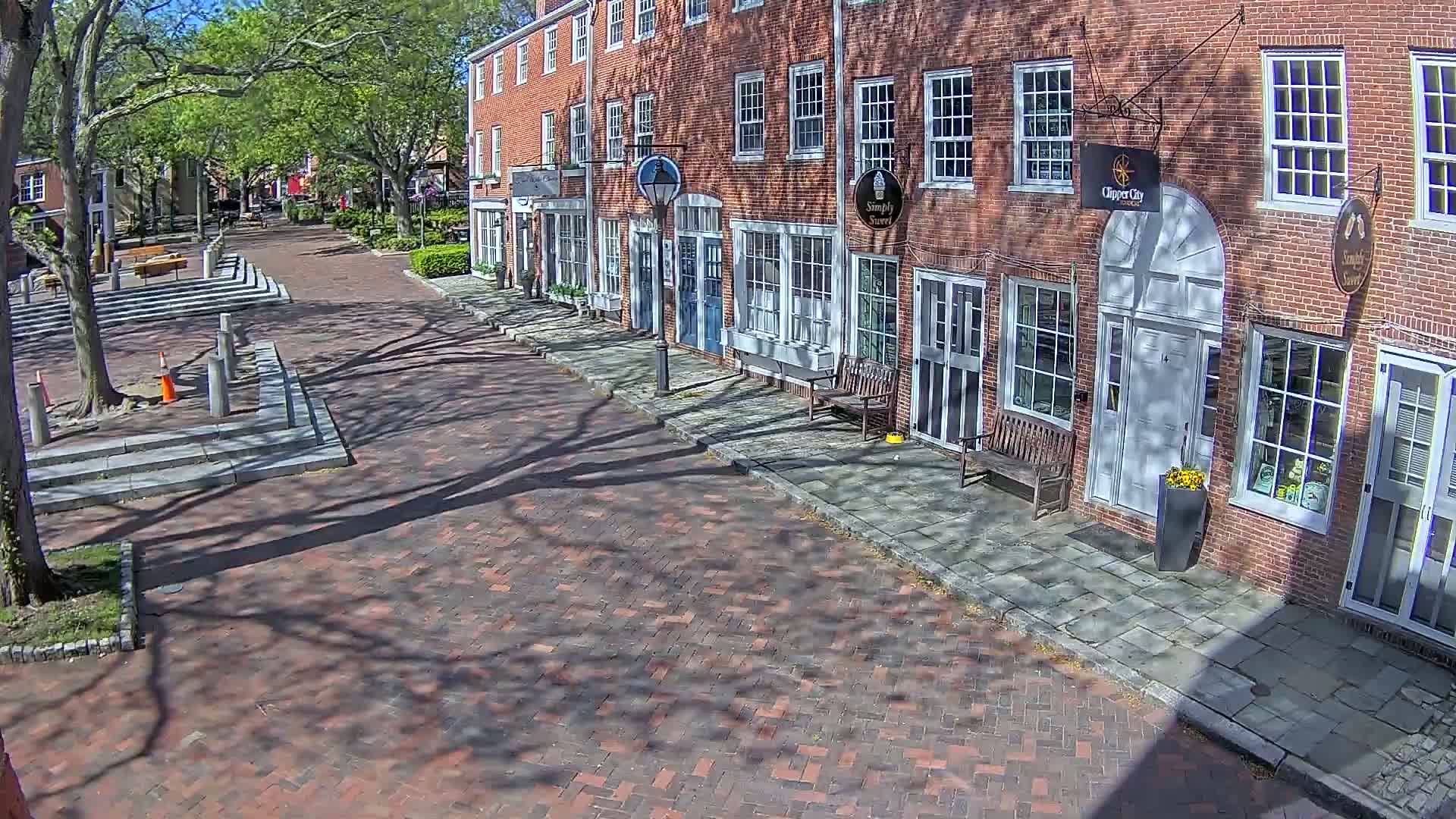 A brick street lined with brick buildings under a sunny sky with tree shadows cast on the street and sidewalks.