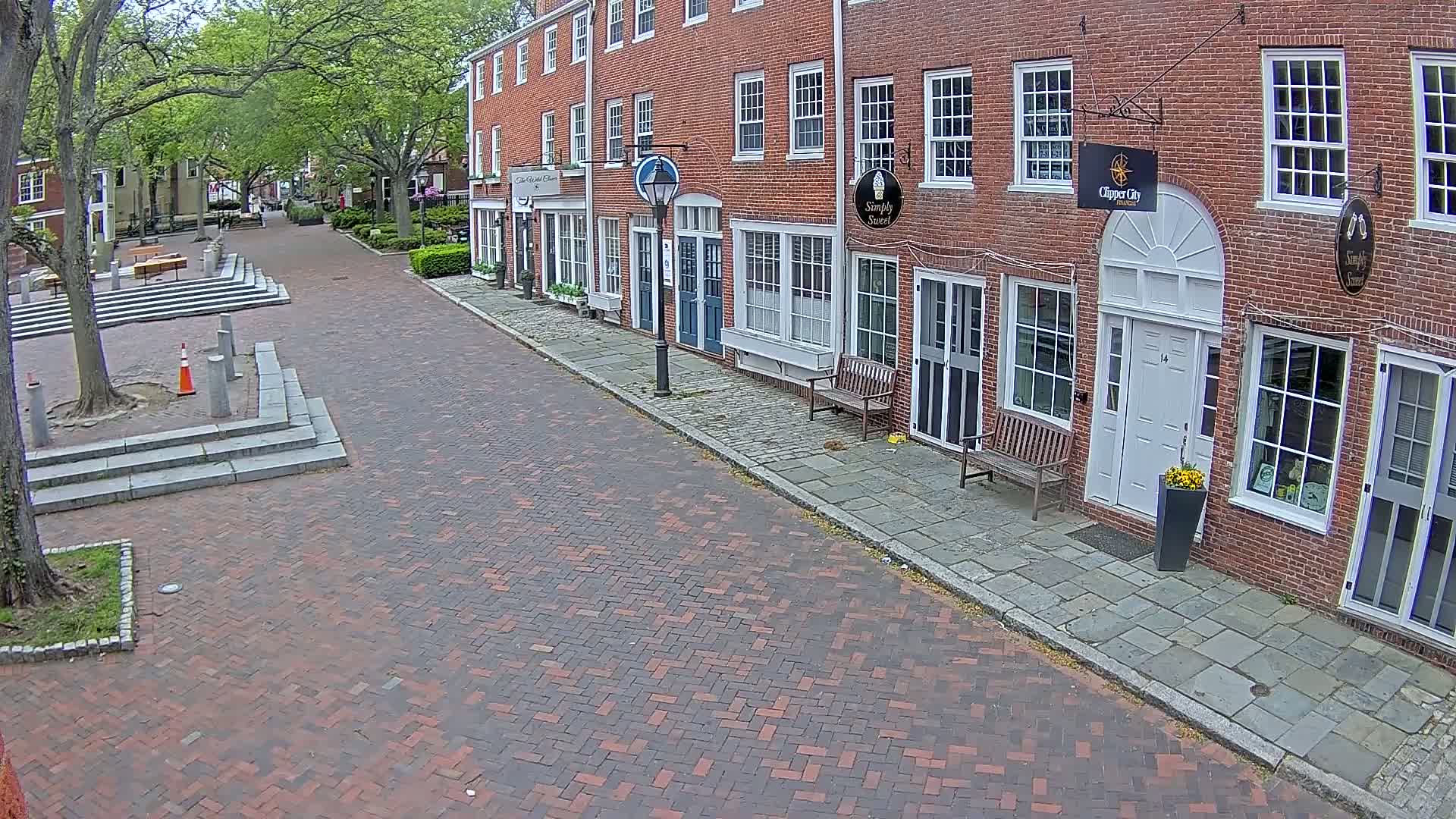 A brick-paved street lined with brick buildings on a partly sunny day.