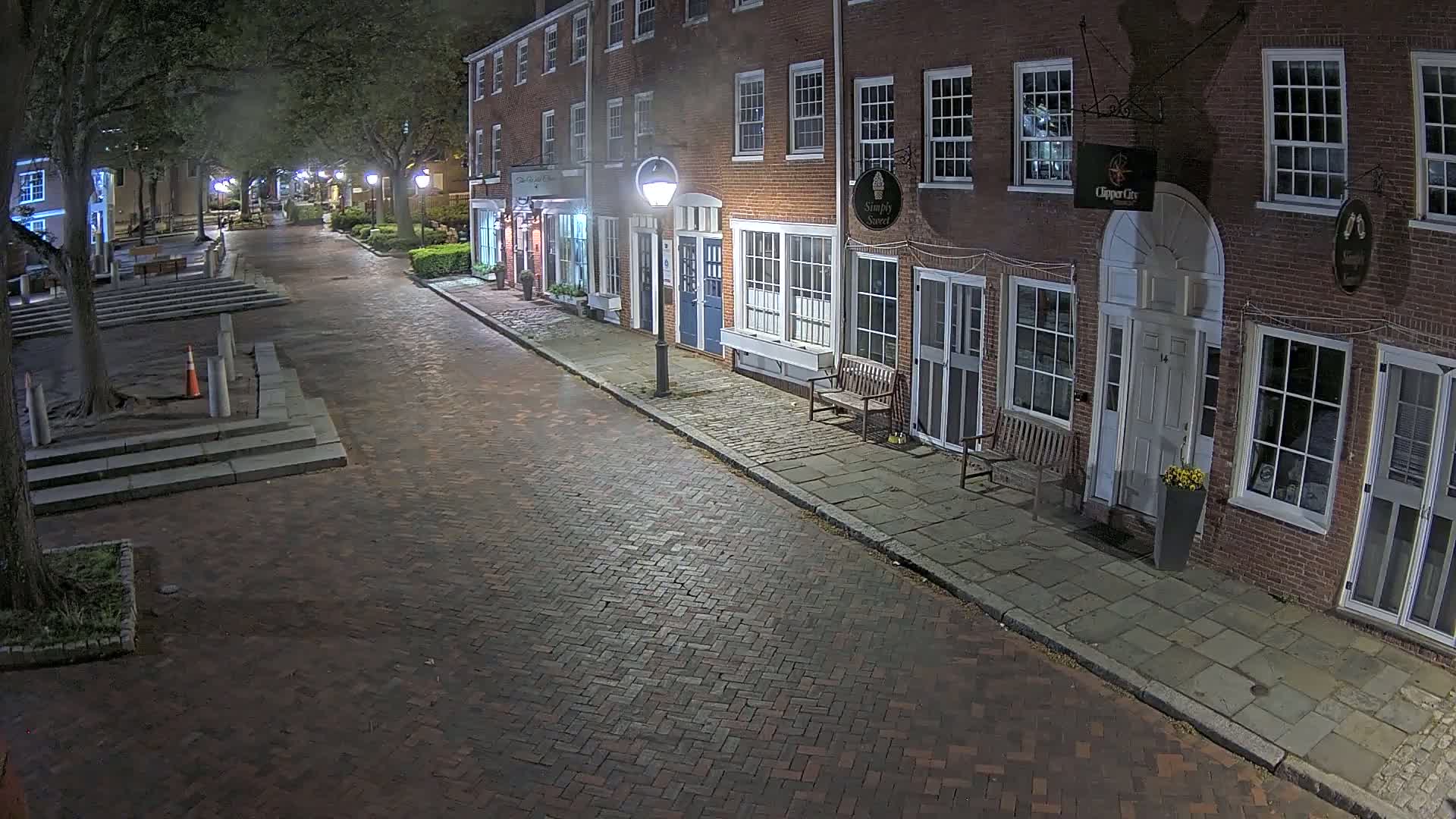 A brick-paved street at night, lined with brick buildings, is illuminated by streetlights under a hazy sky.