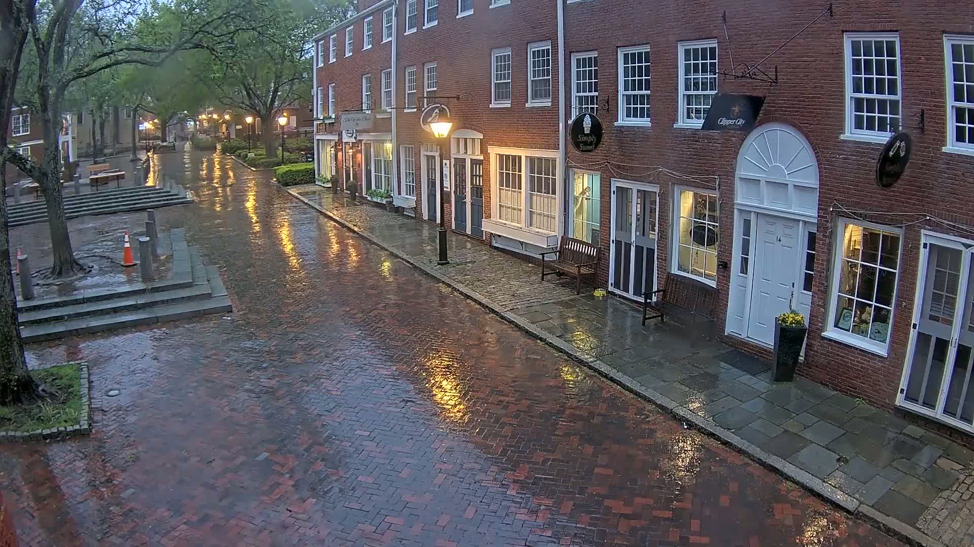 A rain-slicked brick street lined with brick buildings and trees under a cloudy sky.