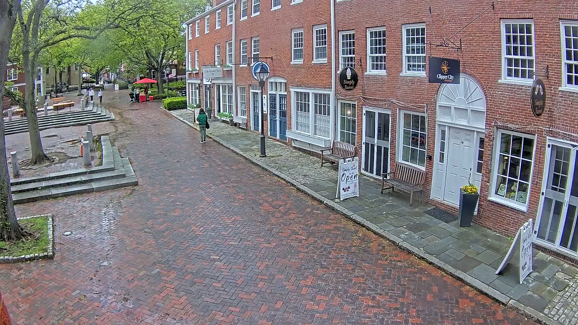 A person walks down a brick-paved street lined with brick buildings on a lightly overcast day.