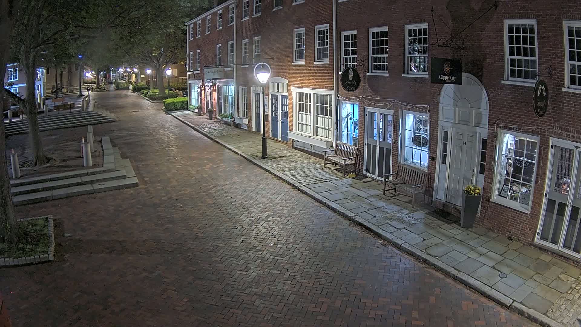A brick street lined with brick buildings at night, lit by street lamps.