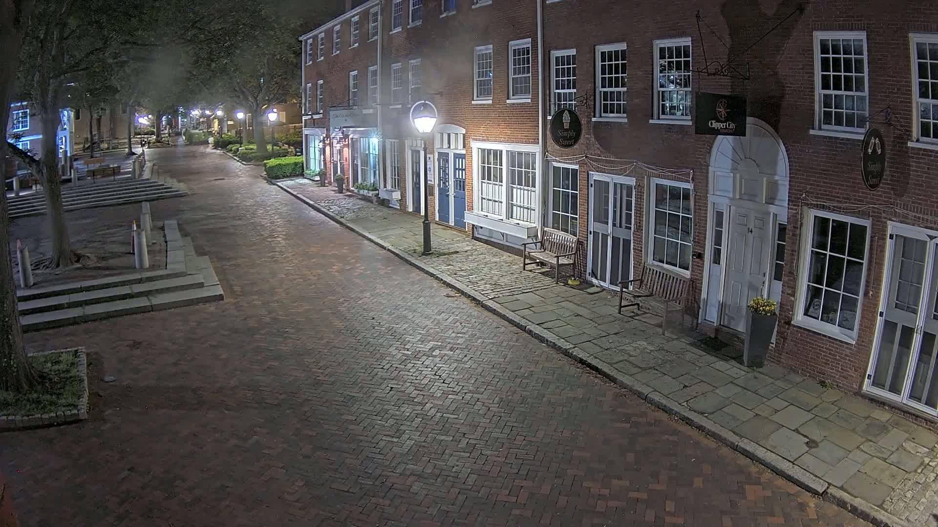 A brick street at night, lined with brick buildings, is illuminated by streetlights under a clear, dark sky.