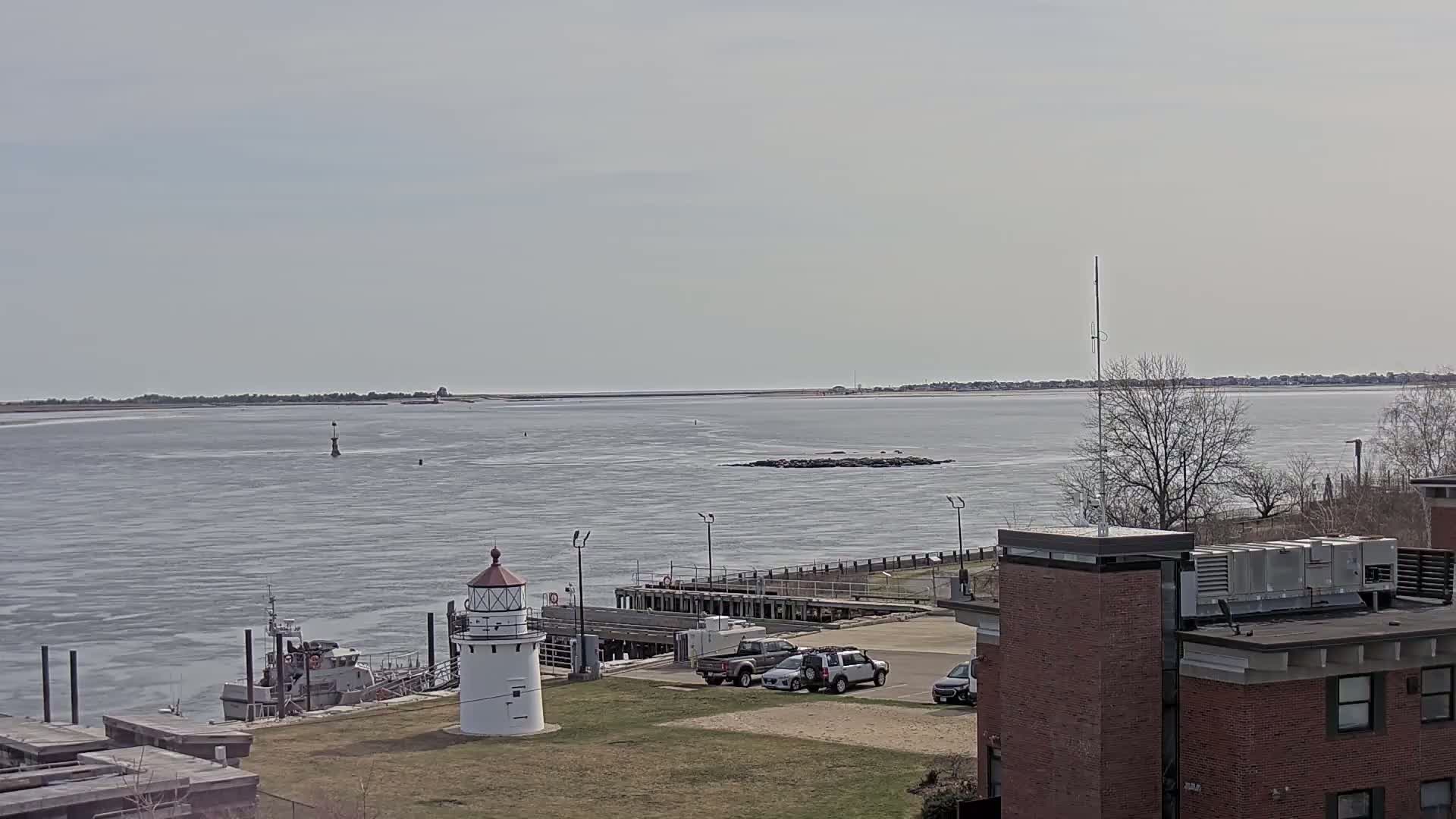 A small white lighthouse stands near a dock and a calm body of water under a mostly cloudy sky.