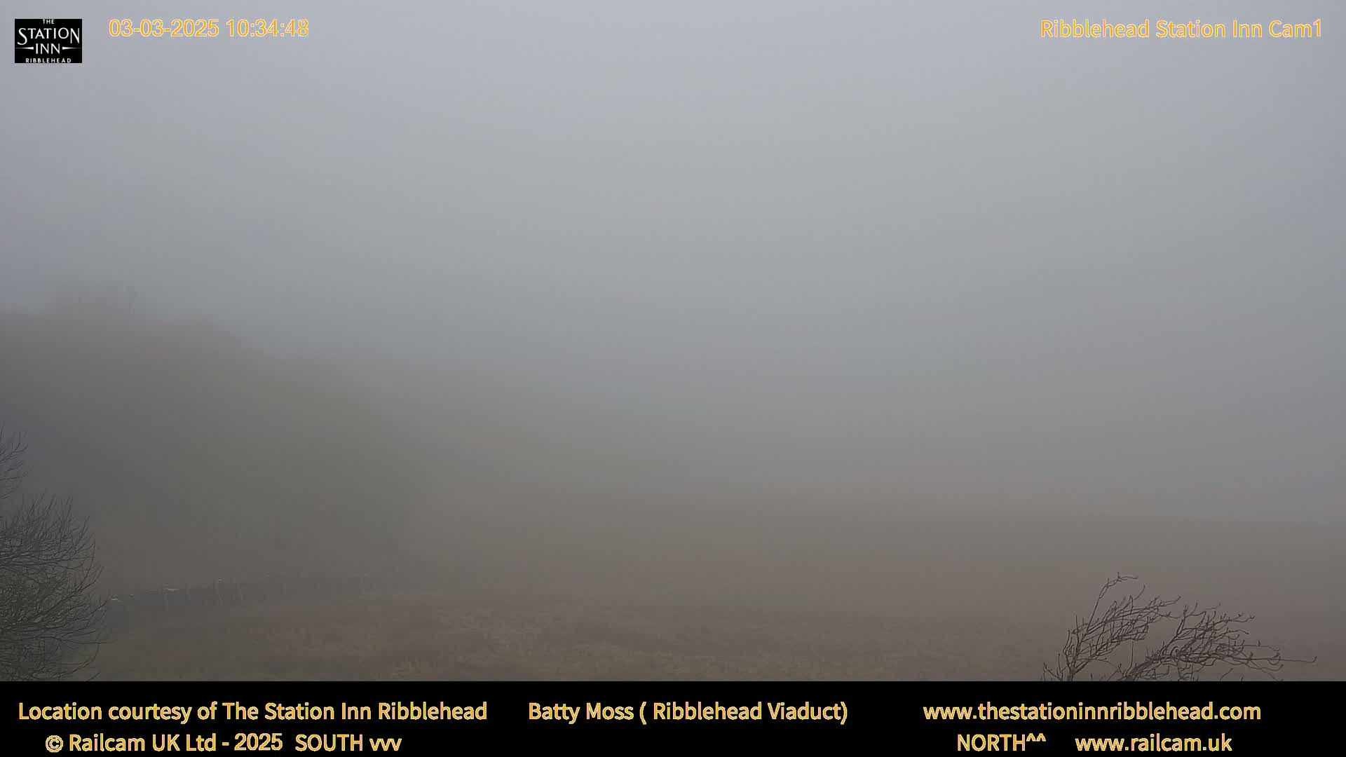 A thick fog obscures a flat, brown landscape with sparse, dark vegetation.