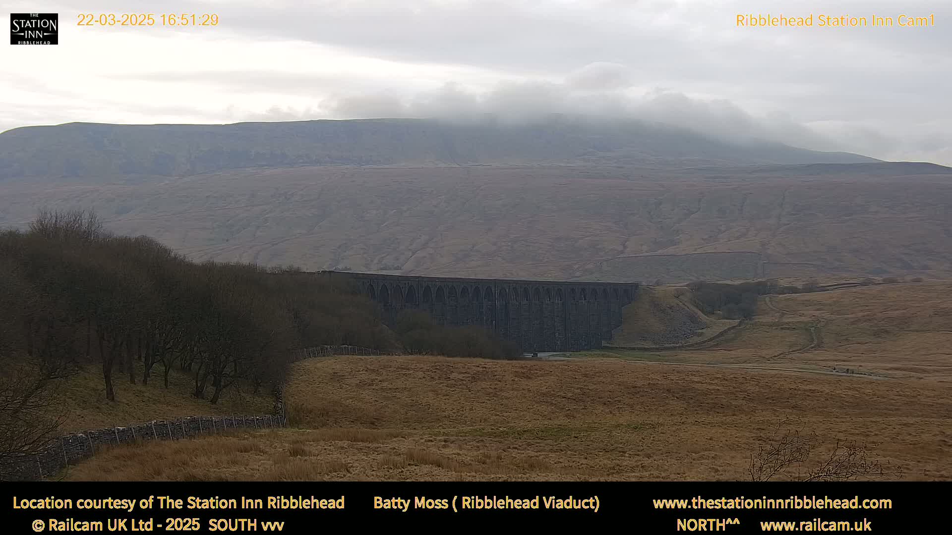 A long stone viaduct sits in a valley below a hazy, overcast mountain range.