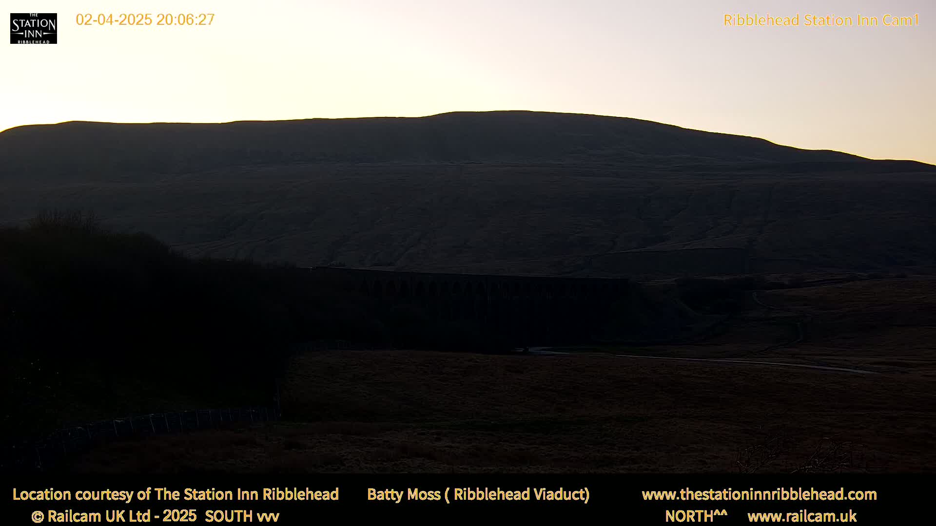 A dark, silhouetted hill and viaduct are visible under a twilight sky.