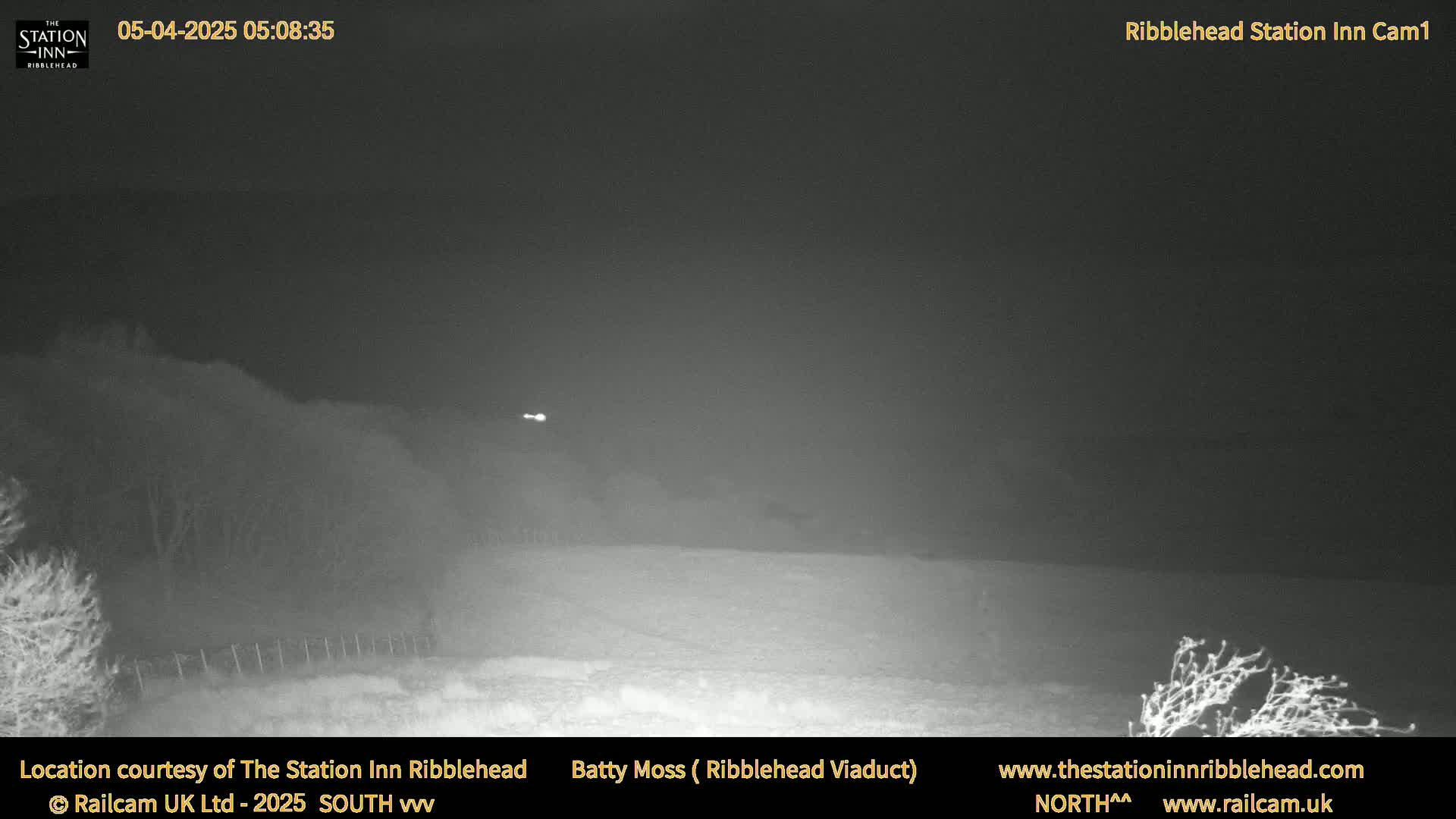 A nighttime, low-light outdoor scene shows a flat, snow-covered landscape under a dark, overcast sky.