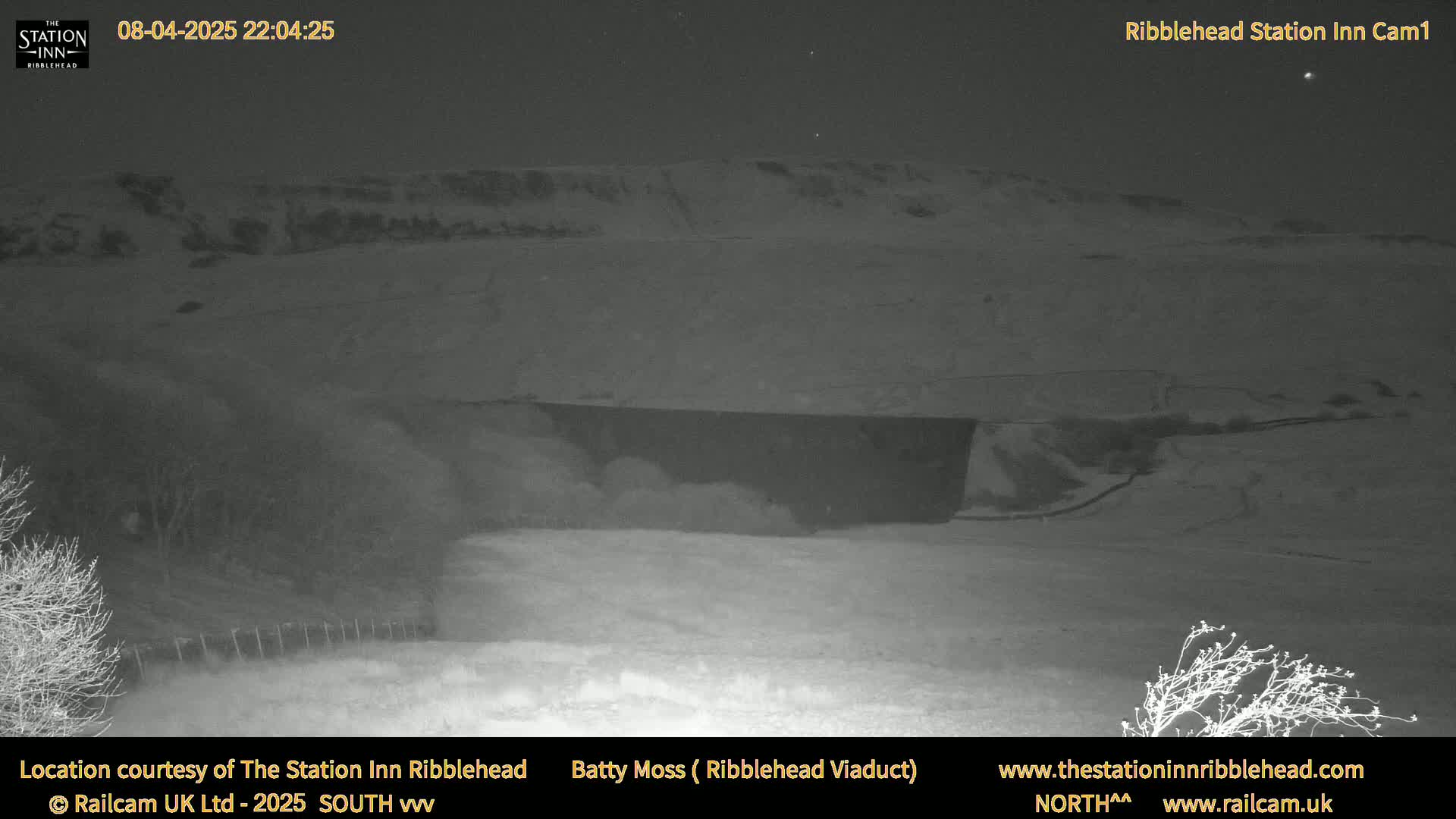 A snow-covered landscape is visible at night, with a dark structure in the midground and a hill in the background under a clear, starry sky.