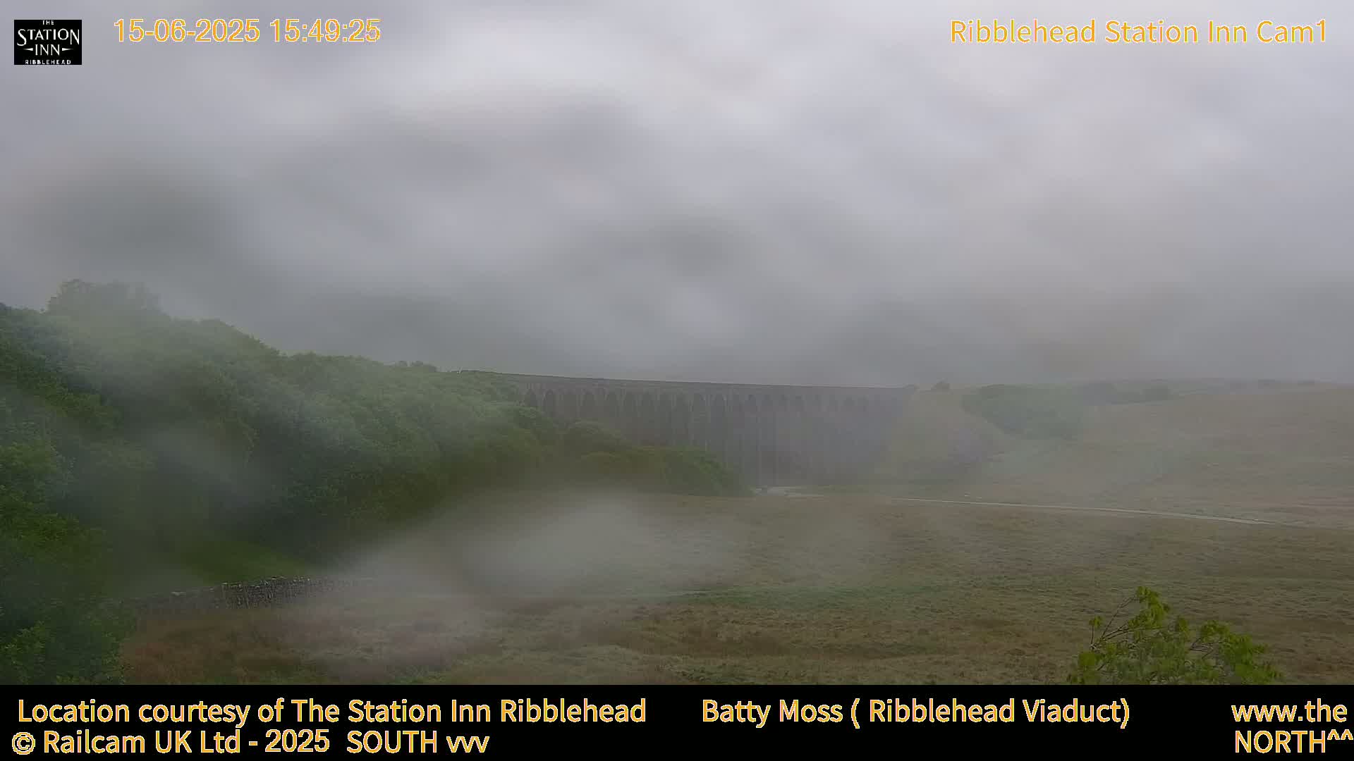 A large stone viaduct is partially obscured by fog over a grassy landscape.