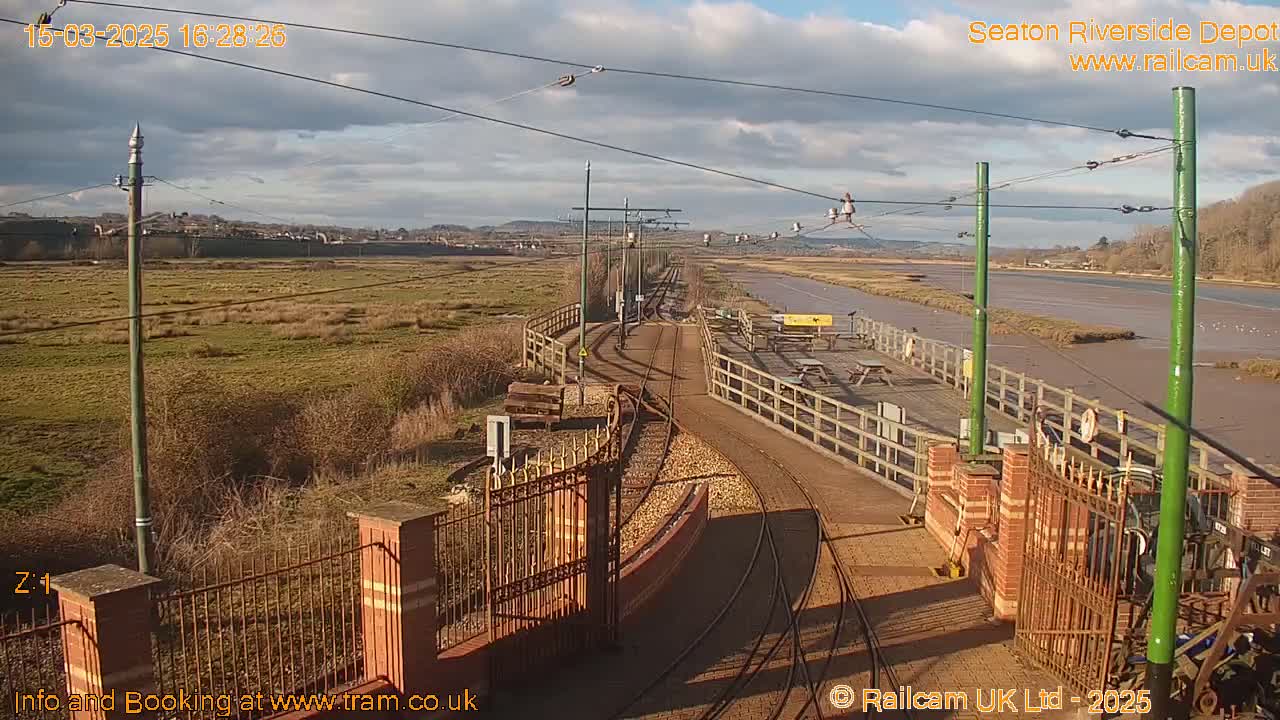 A sunny day overlooking a railway depot and a river, with grassy fields and a partly cloudy sky.