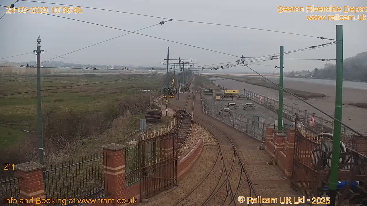 A train depot with railway tracks curving towards a river under an overcast sky.