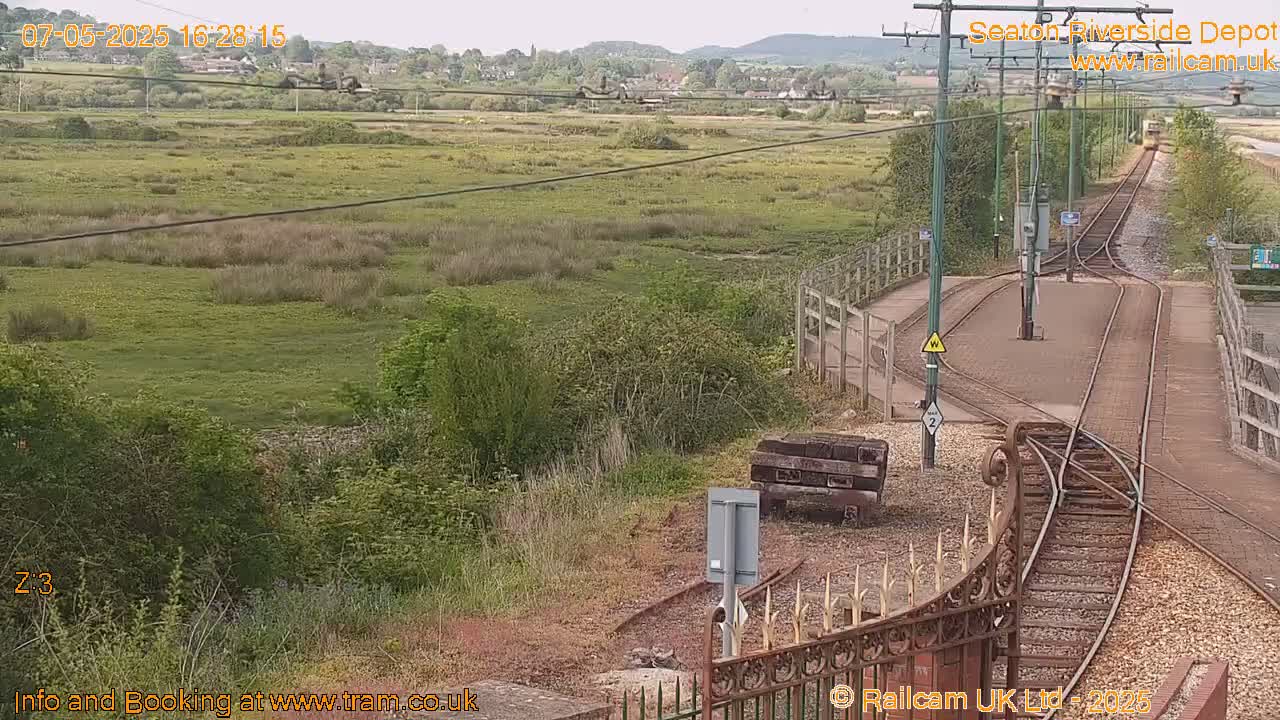 A train depot with a grassy field and distant hills under a partly cloudy sky.