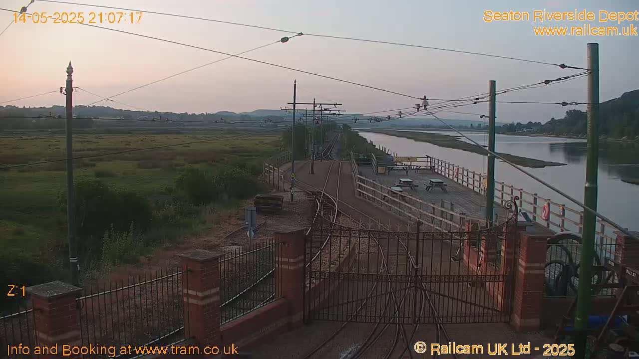 A twilight view of a railway depot alongside a calm river, with grassy marshland visible in the background.