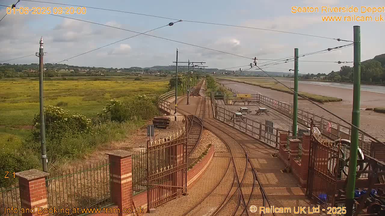 A sunny day at a train depot with tracks curving toward a waterway bordered by grassy fields.
