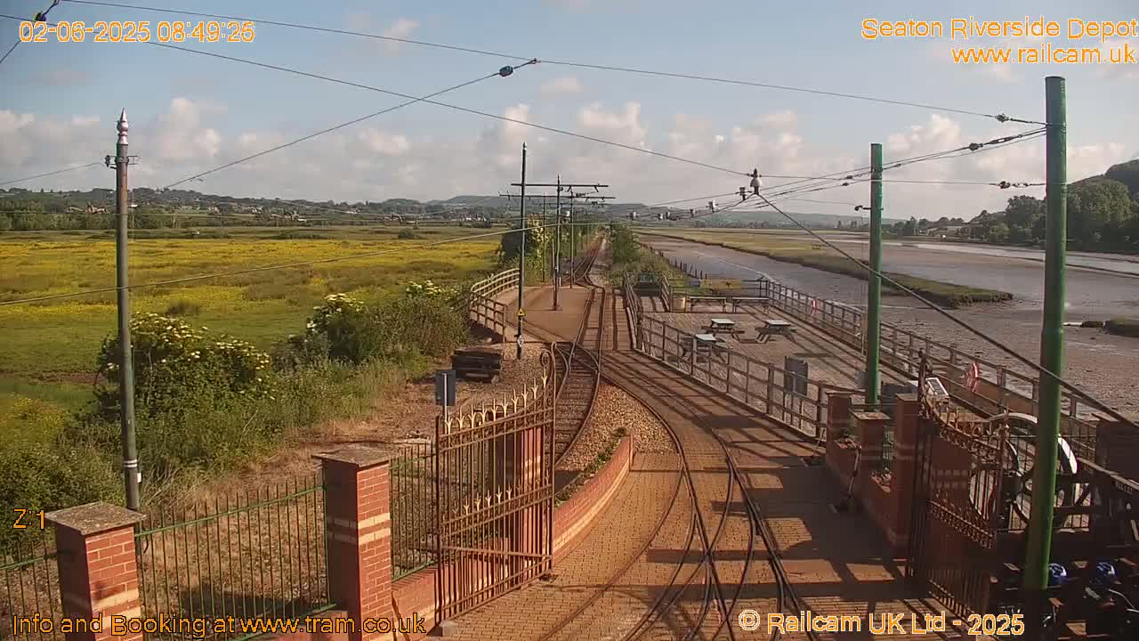 A sunny day at a railway depot with a view of a waterway and a field of yellow flowers.