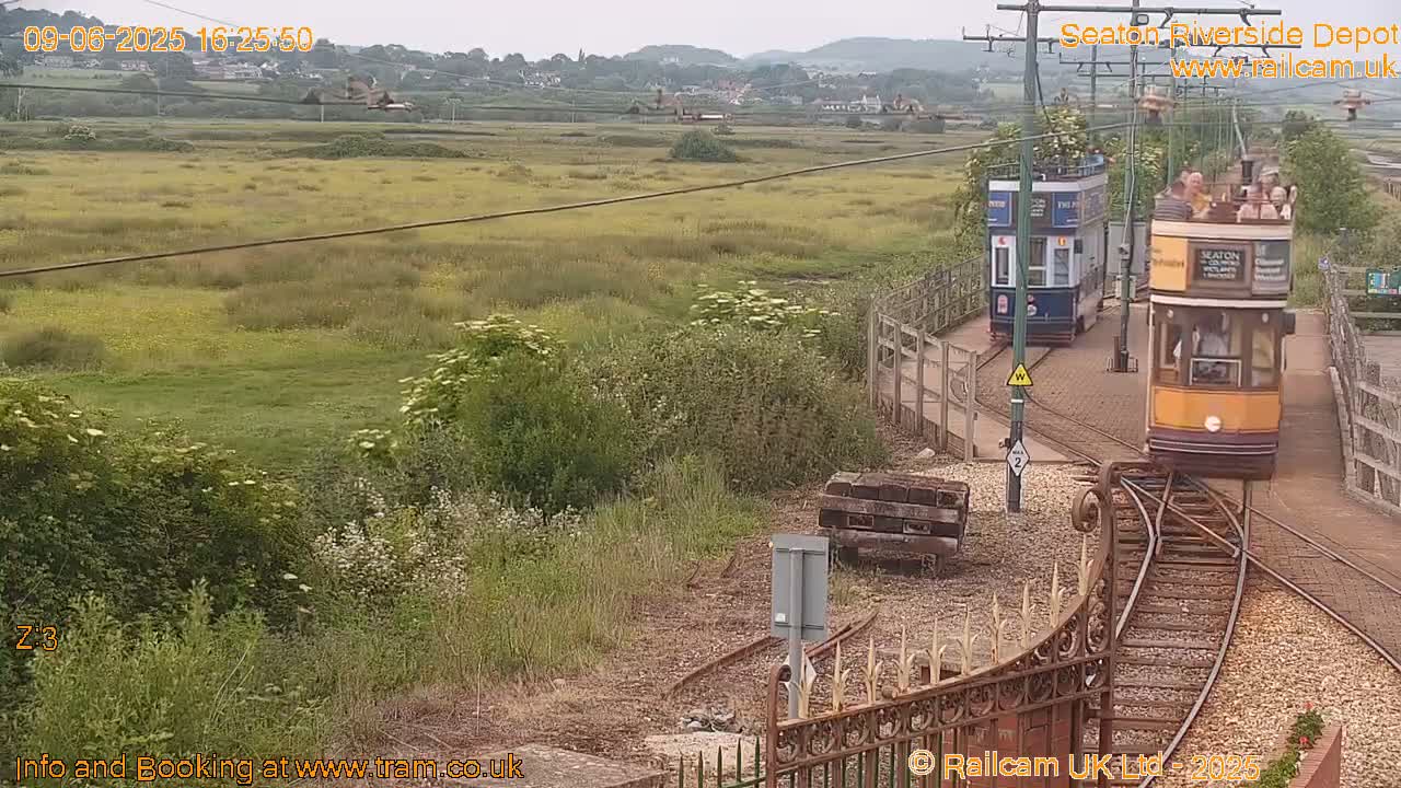 Two vintage trams are on a railway line next to a grassy field under an overcast sky.