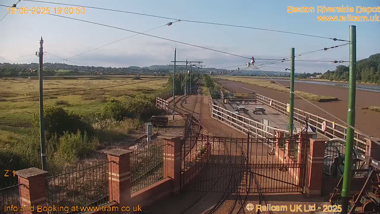 A train depot with railway tracks and a wooden platform overlooks a marshy expanse under a clear, sunny sky.