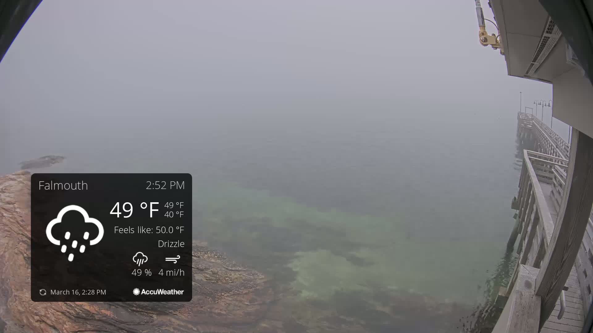 A foggy, drizzly day shows a long wooden pier extending over shallow, partially visible water.
